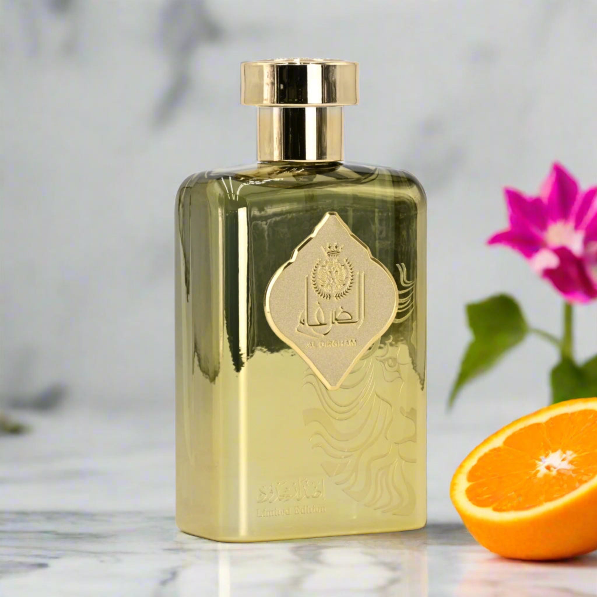 Gold perfume bottle with a decorative label on a marble surface with an orange and flower in the background.