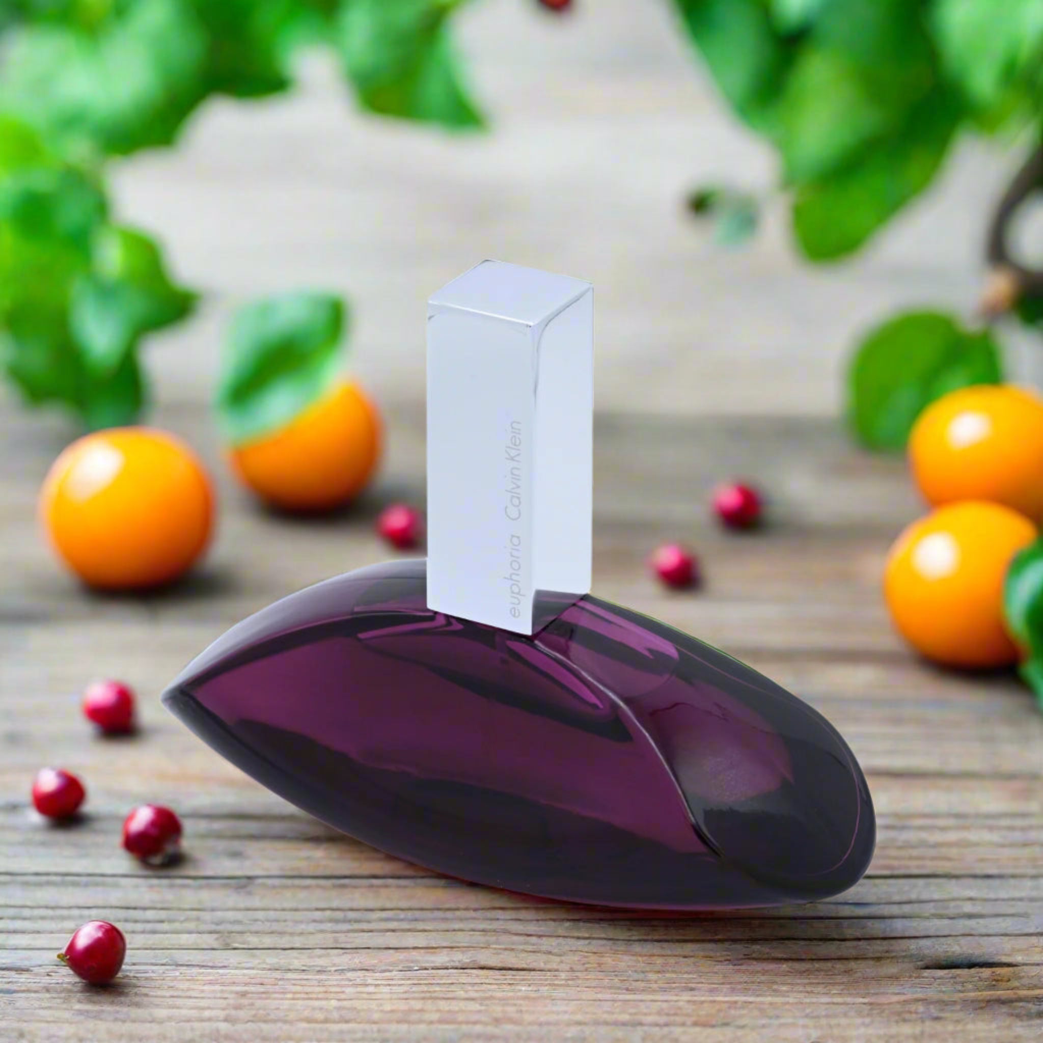 Perfume bottle with a white cap on a wooden surface with fruits and leaves in the background