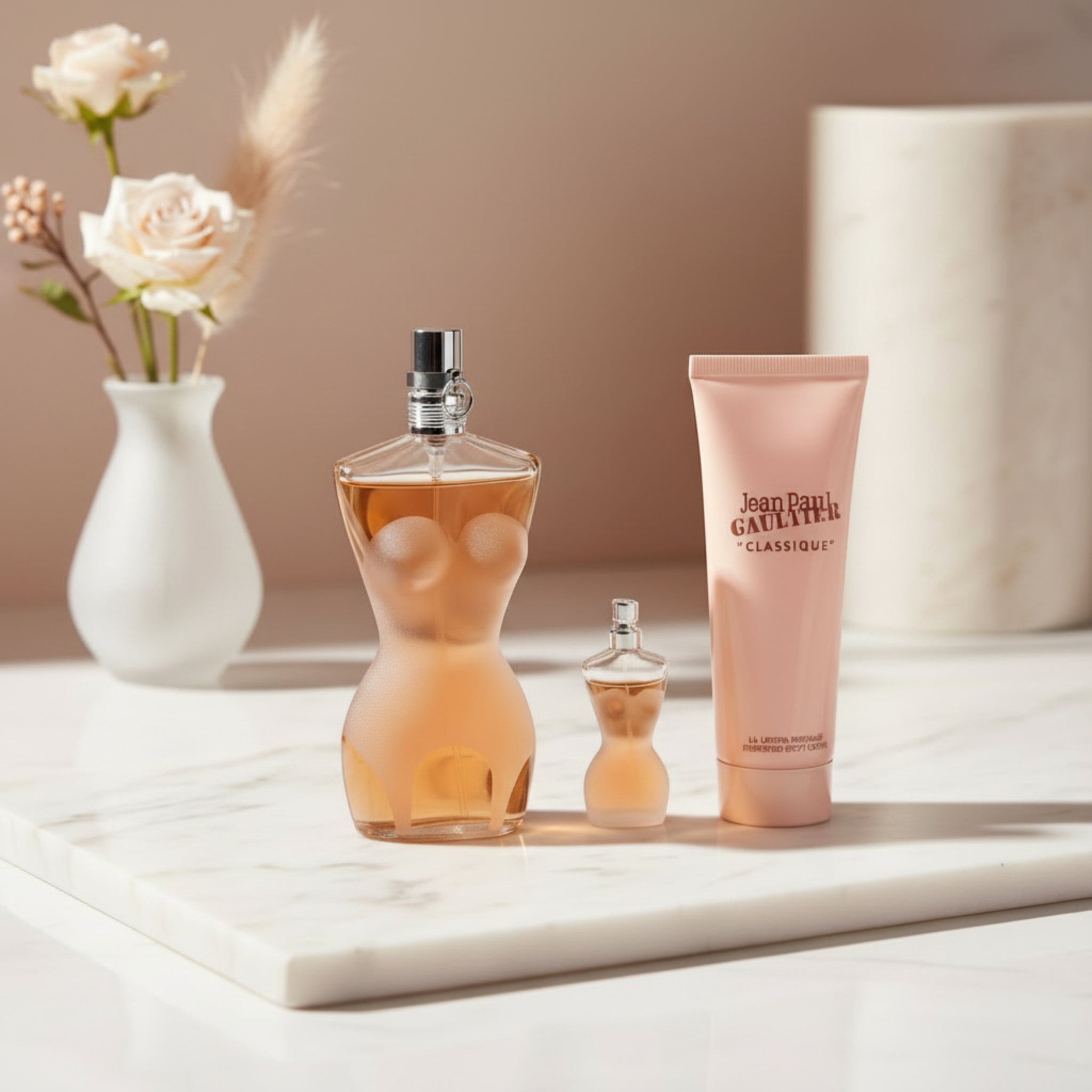 Two perfume bottles and a tube of Jean Paul Gaultier Classique on a white background