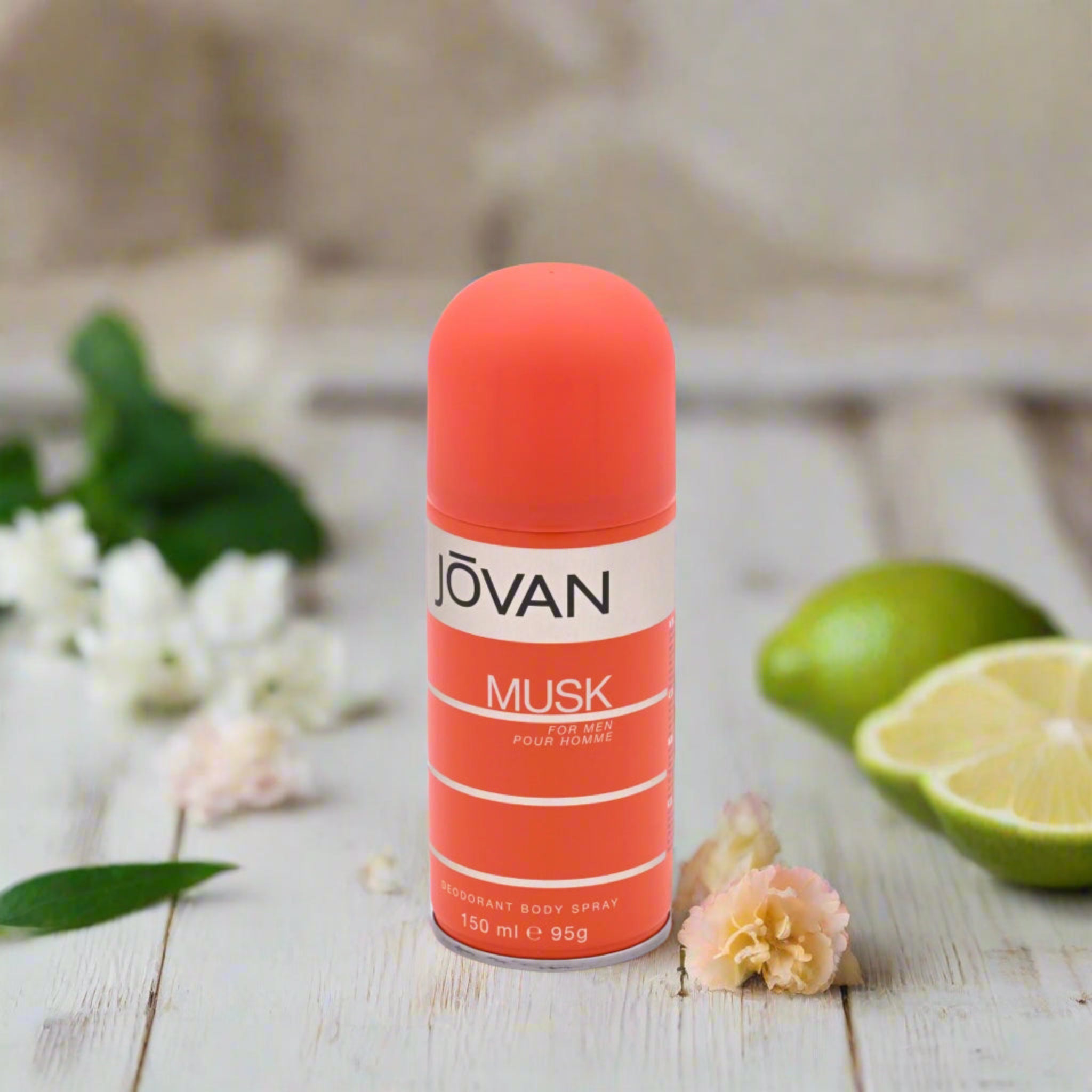 Jovan Musk deodorant spray can on a wooden surface with flowers and limes in the background