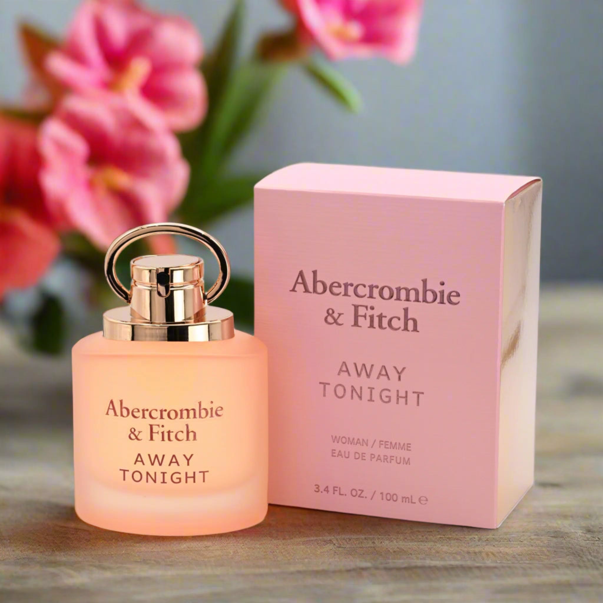 Abercrombie & Fitch perfume bottle and packaging on a wooden surface with pink flowers in the background.