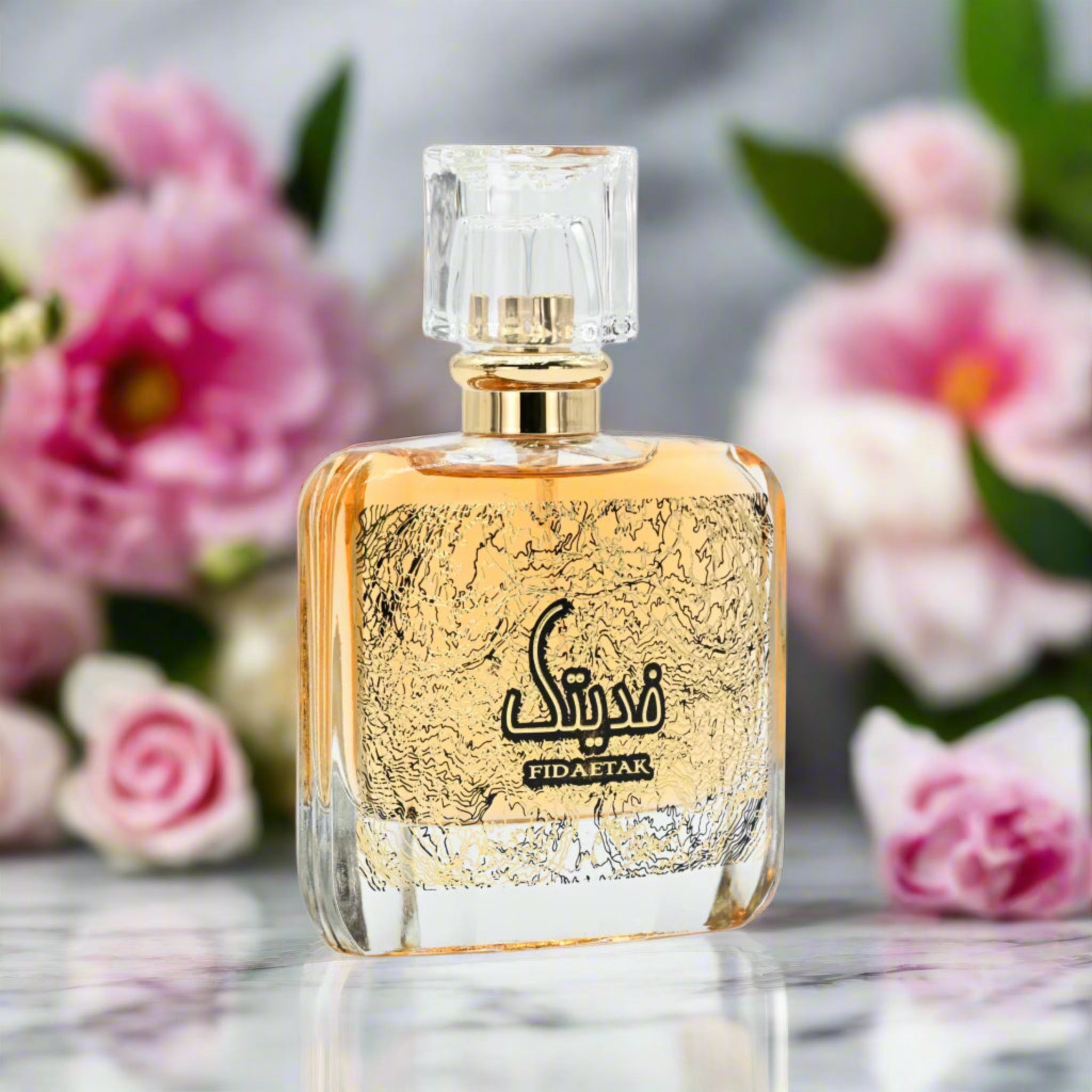 Perfume bottle with gold and black design on a reflective surface with flowers in the background