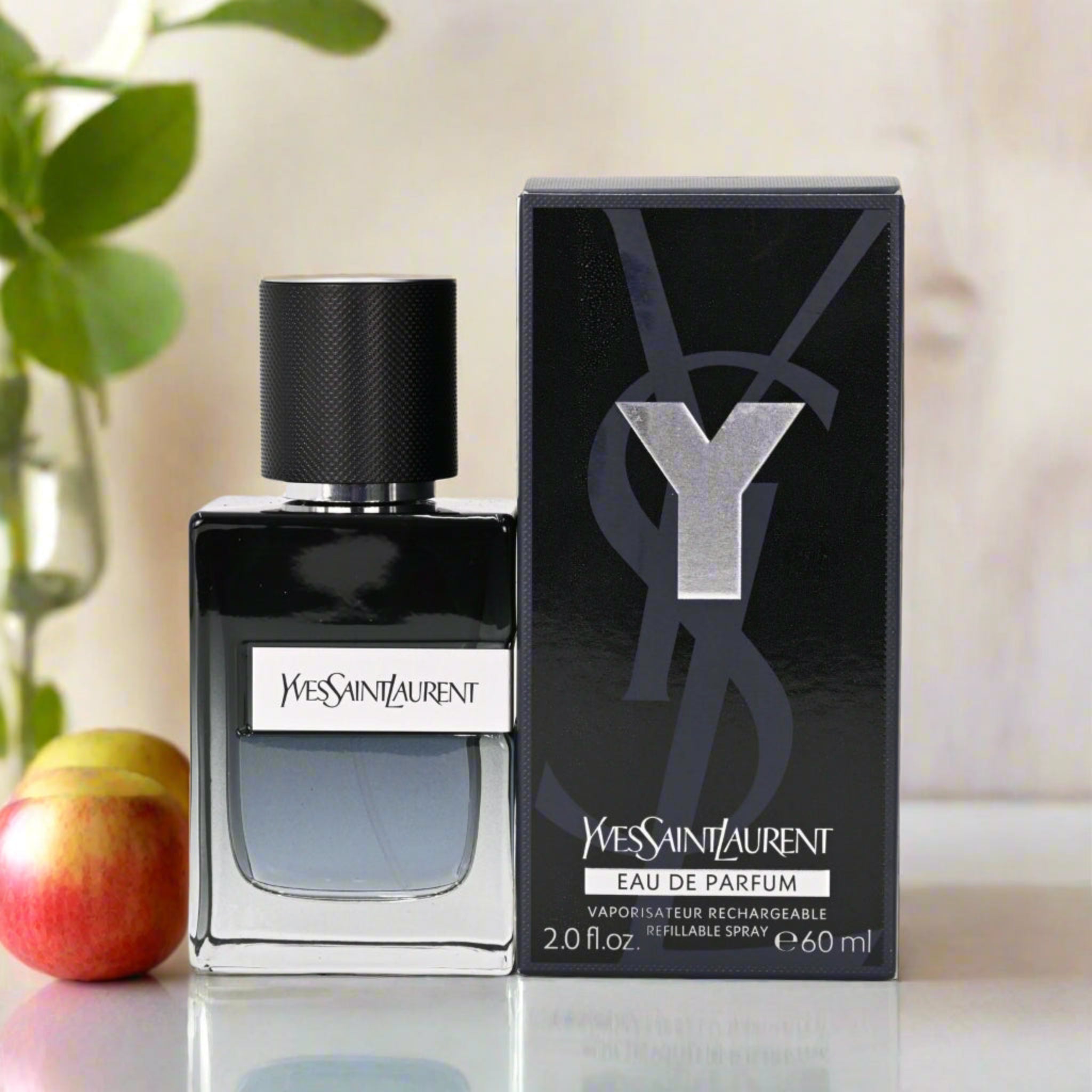 YSL perfume bottle and packaging on a reflective surface with apples and a plant in the background