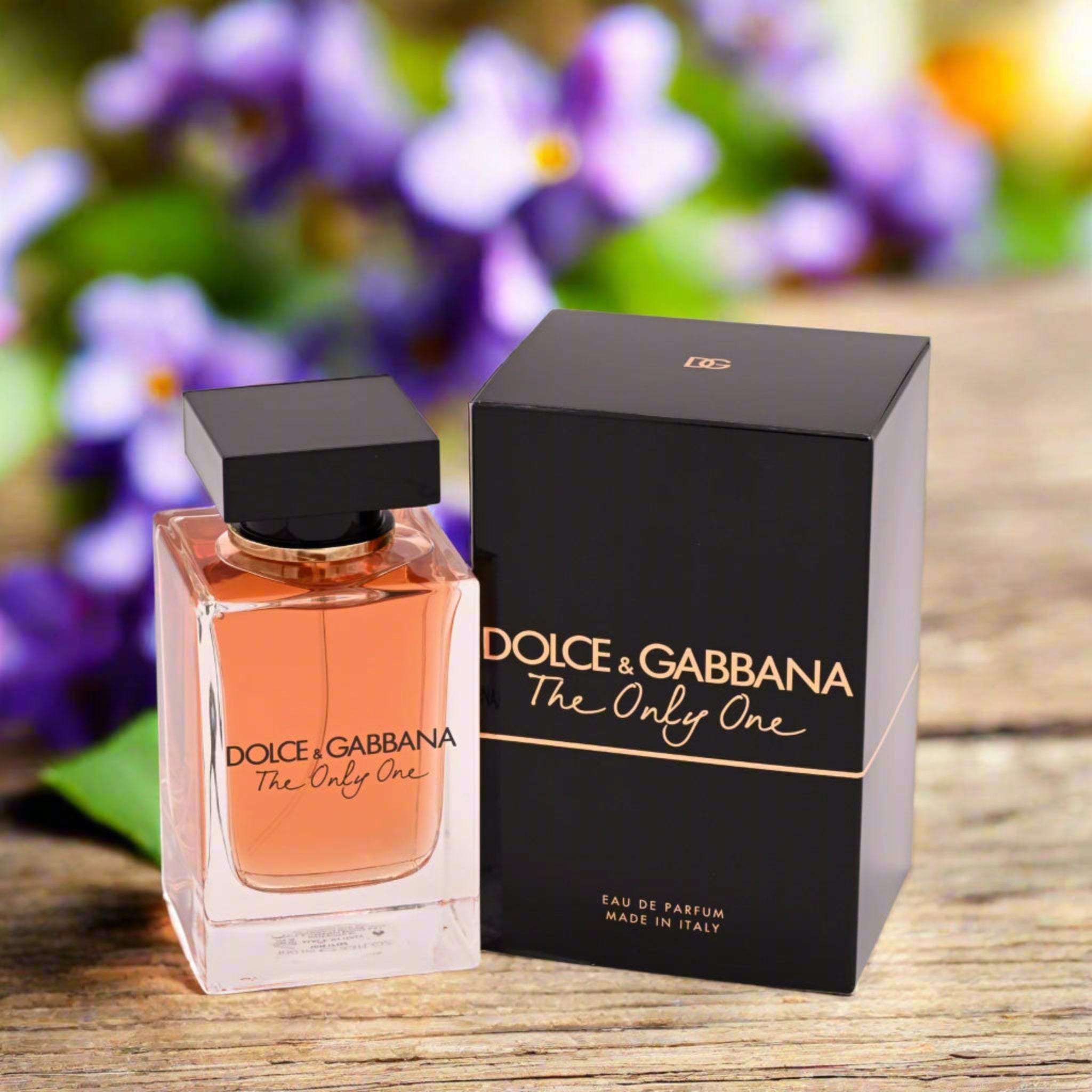 Dolce & Gabbana perfume bottle and packaging on a wooden surface with flowers in the background