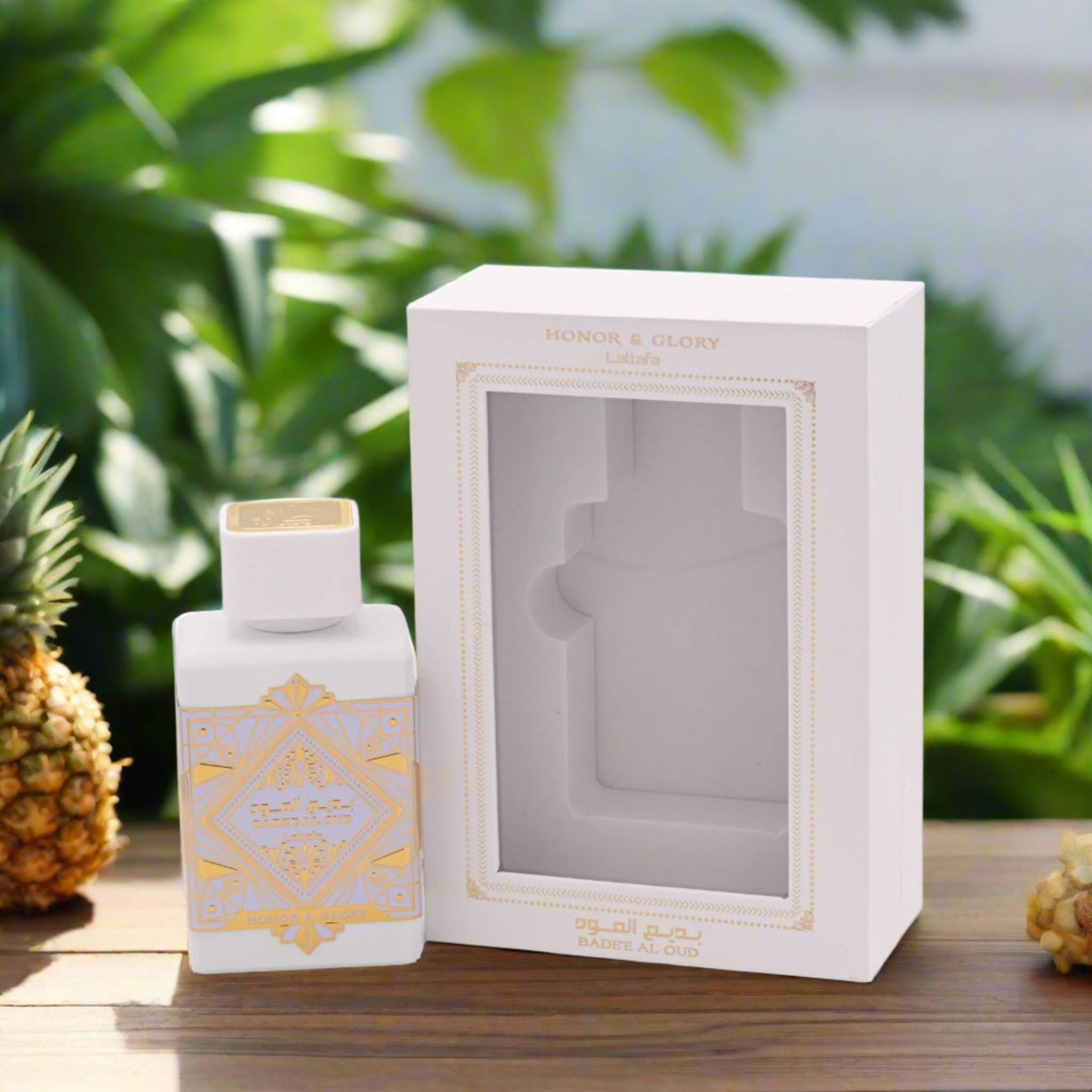White perfume bottle with gold accents and matching box on a wooden surface with greenery in the background