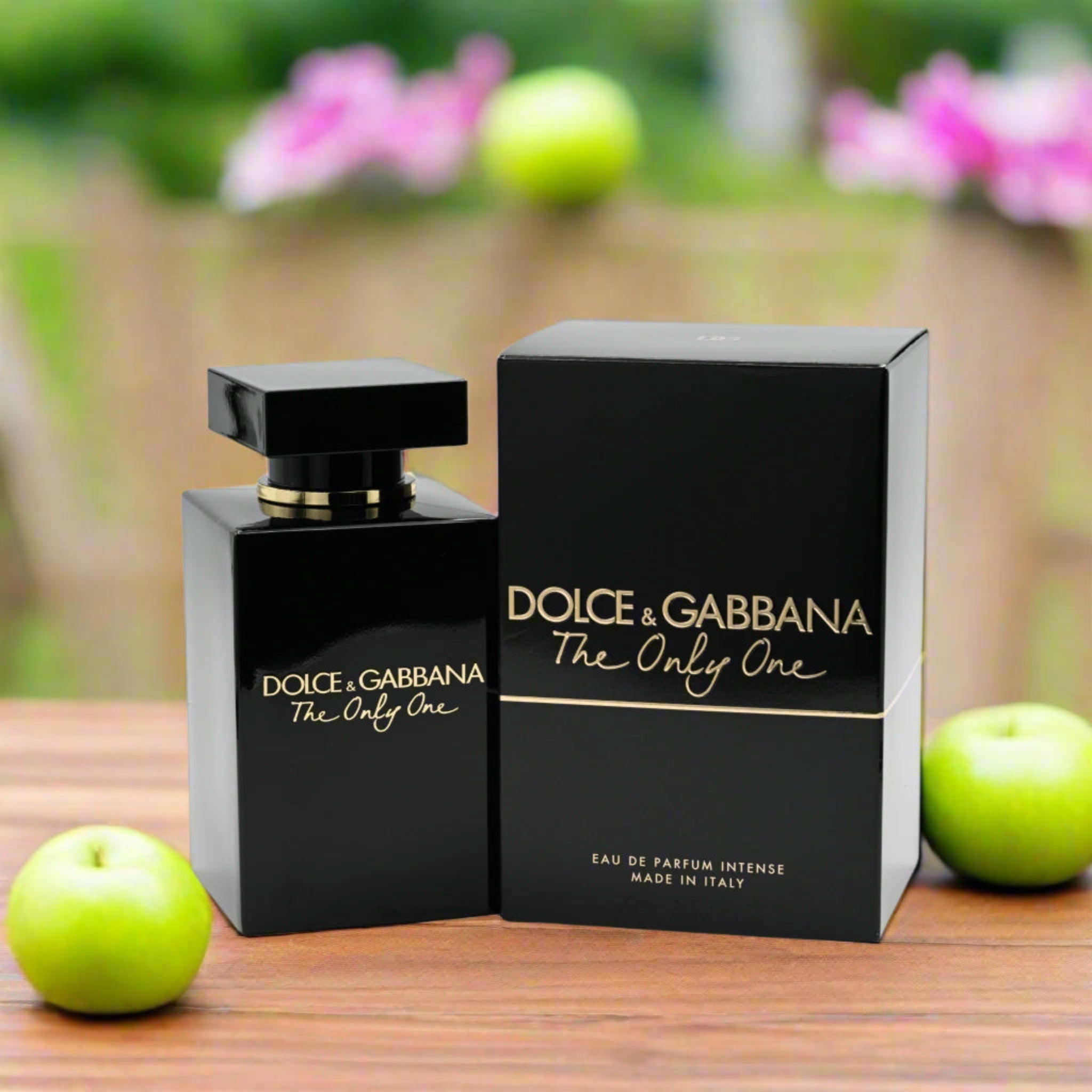 Dolce & Gabbana perfume bottle and packaging on a wooden surface with apples and flowers in the background.