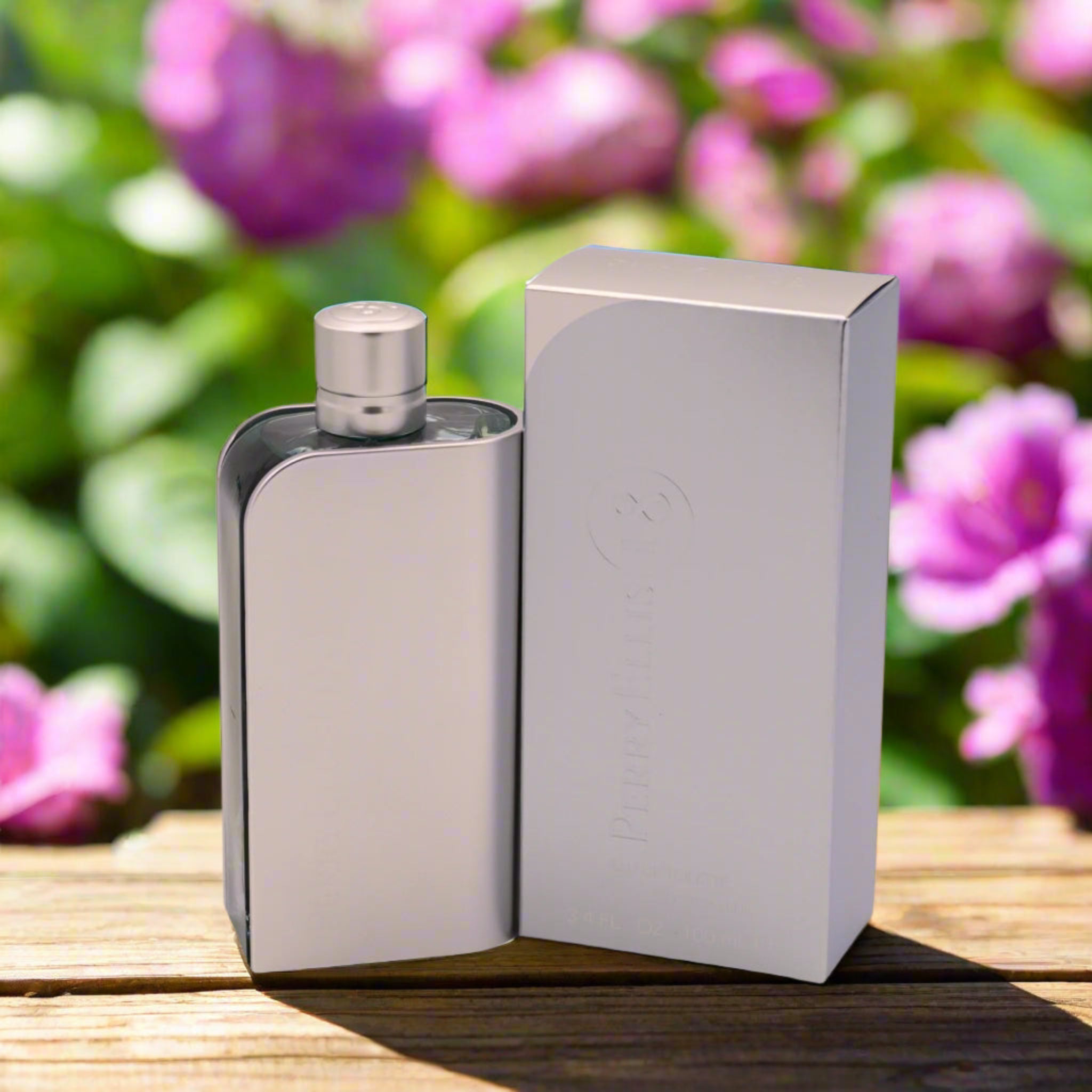Silver flask and box on a wooden surface with pink flowers in the background