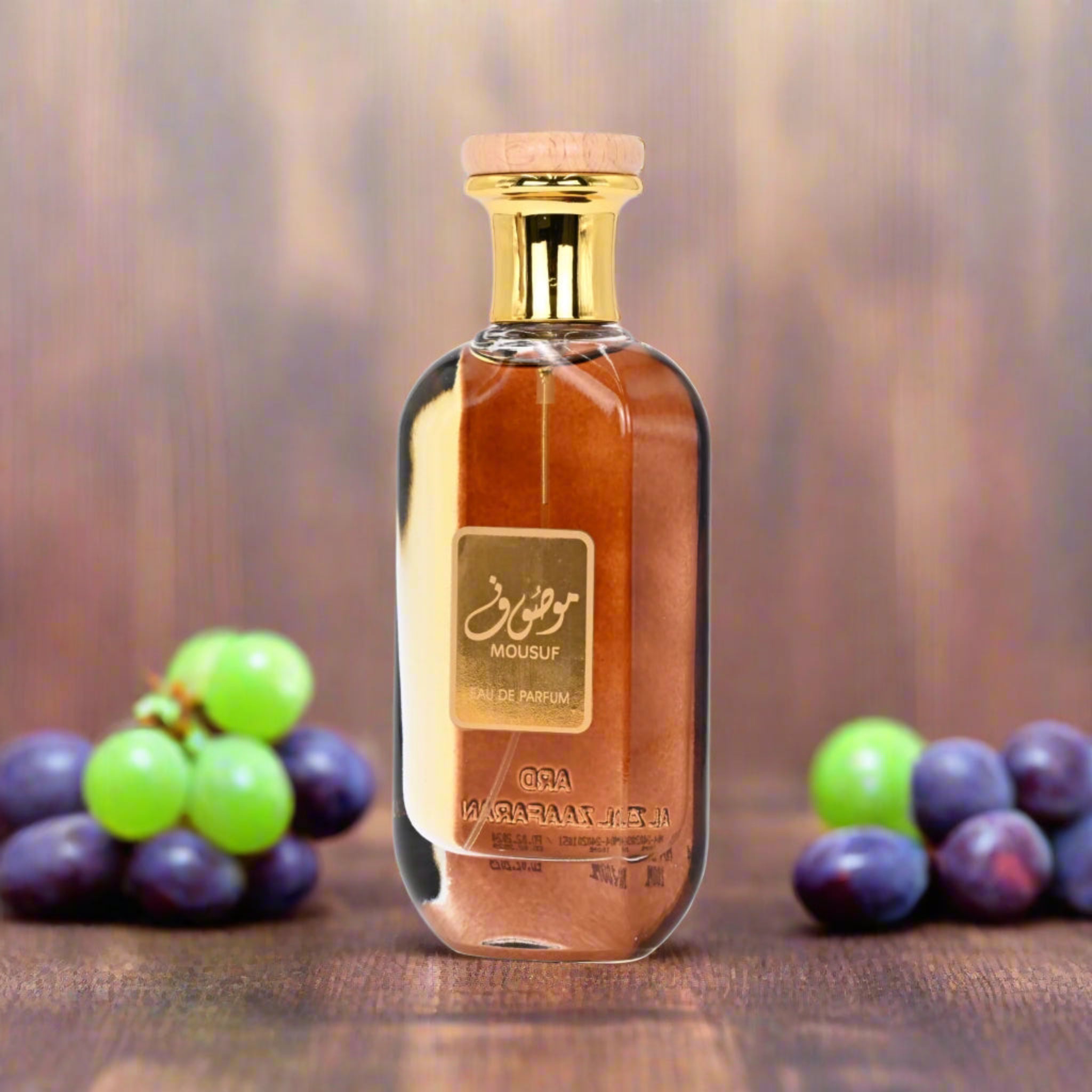 Perfume bottle with gold cap and label, surrounded by grapes on a wooden surface.