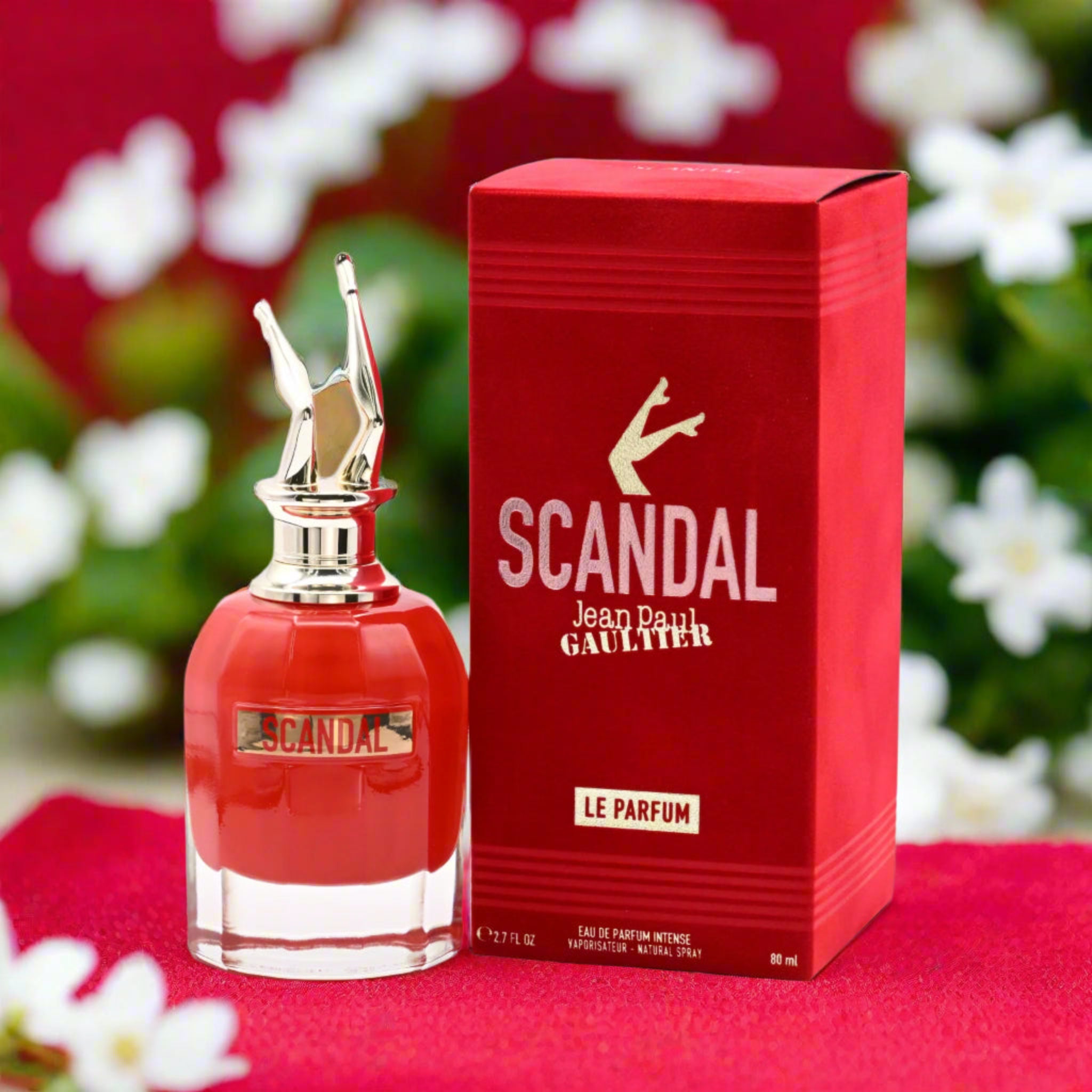 Jean Paul Gaultier Scandal perfume bottle and packaging on a red background with flowers.