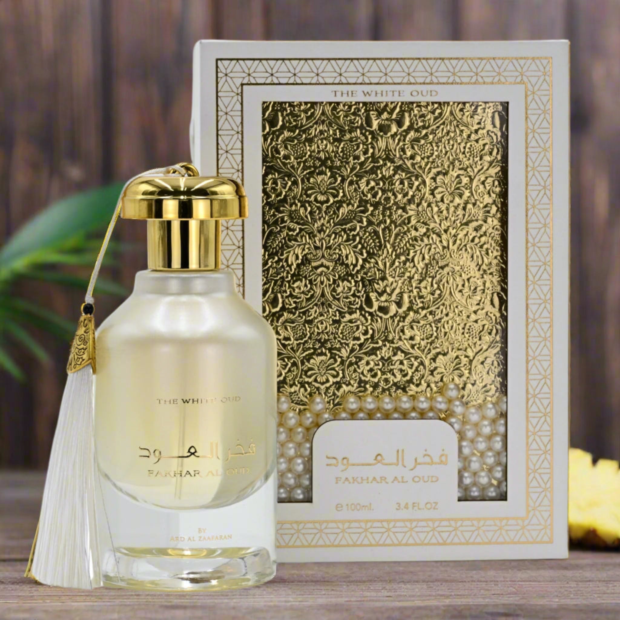 Perfume bottle with gold cap and tassel next to its decorative box on a wooden surface.