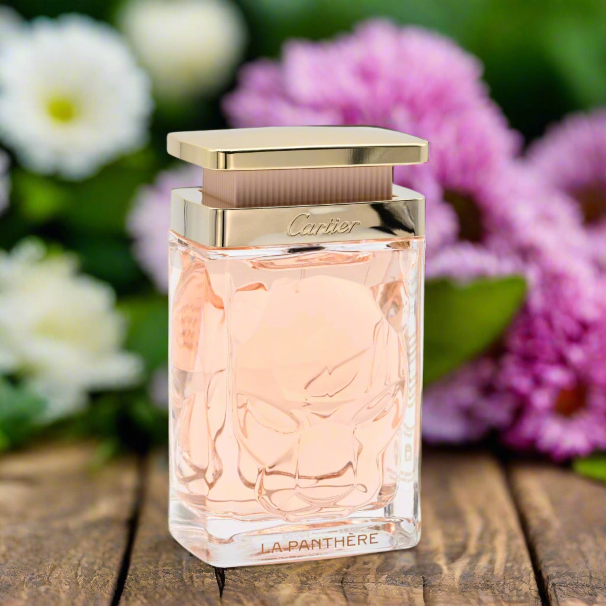 Cartier La Panthere perfume bottle on a wooden surface with flowers in the background