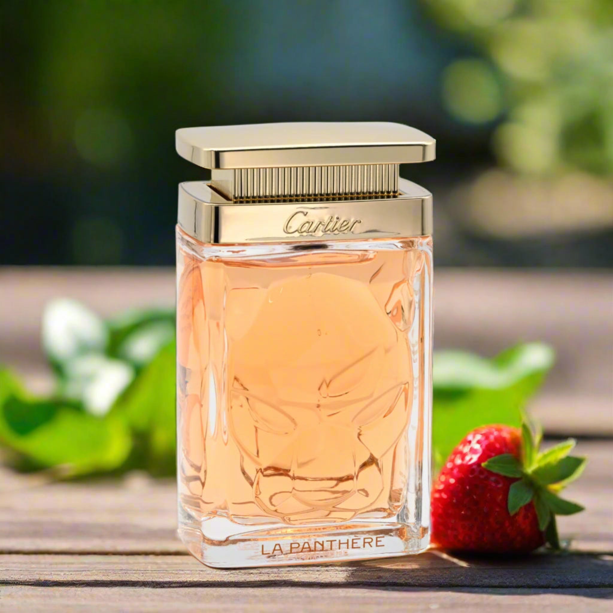 Cartier perfume bottle with a strawberry on a wooden surface