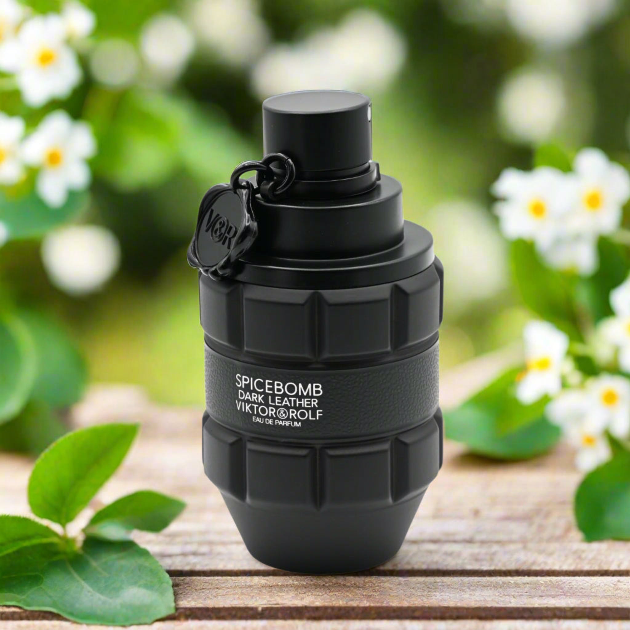 Black grenade-shaped perfume bottle with 'Spicebomb' text on a wooden surface with greenery in the background