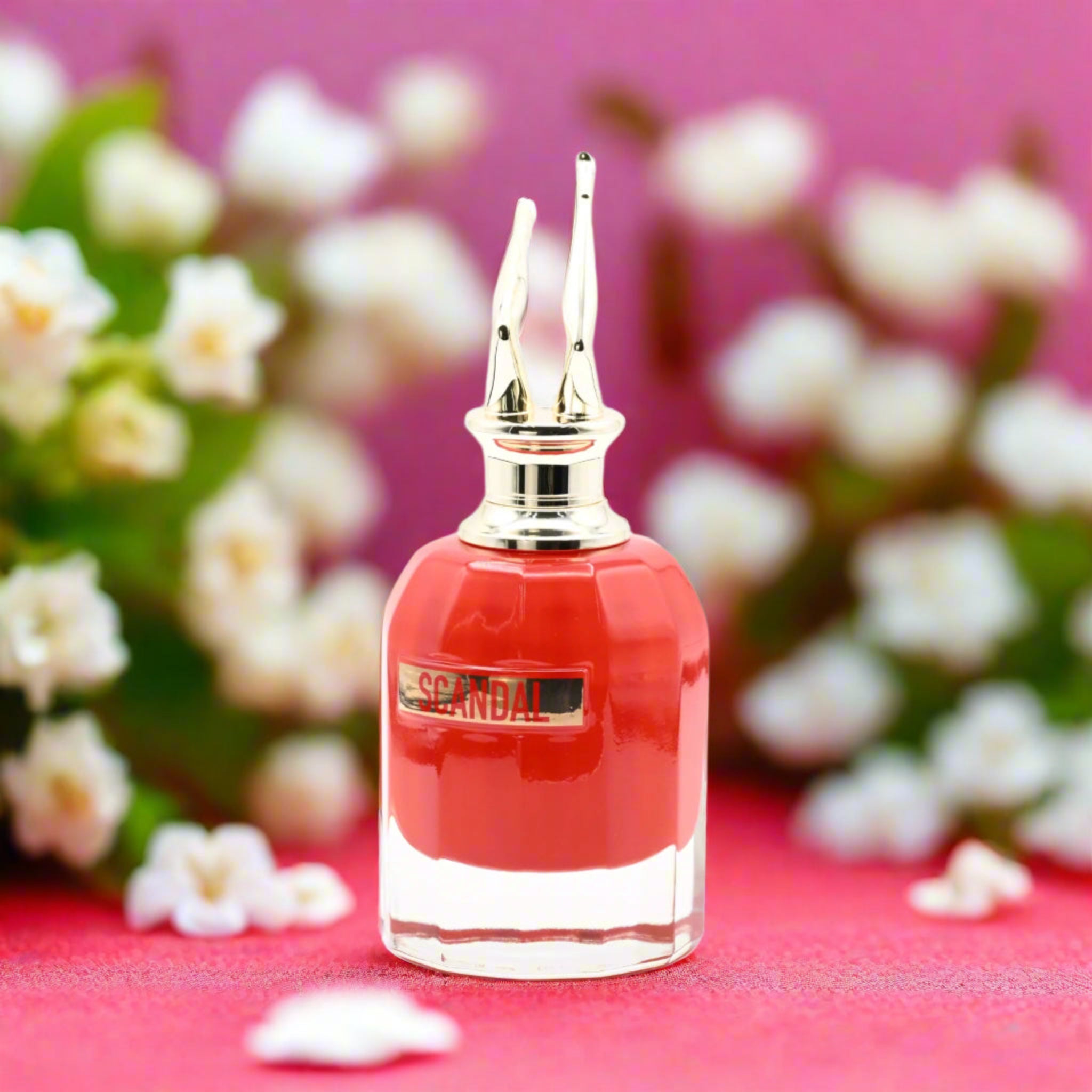 Red perfume bottle with gold cap on a pink background with white flowers
