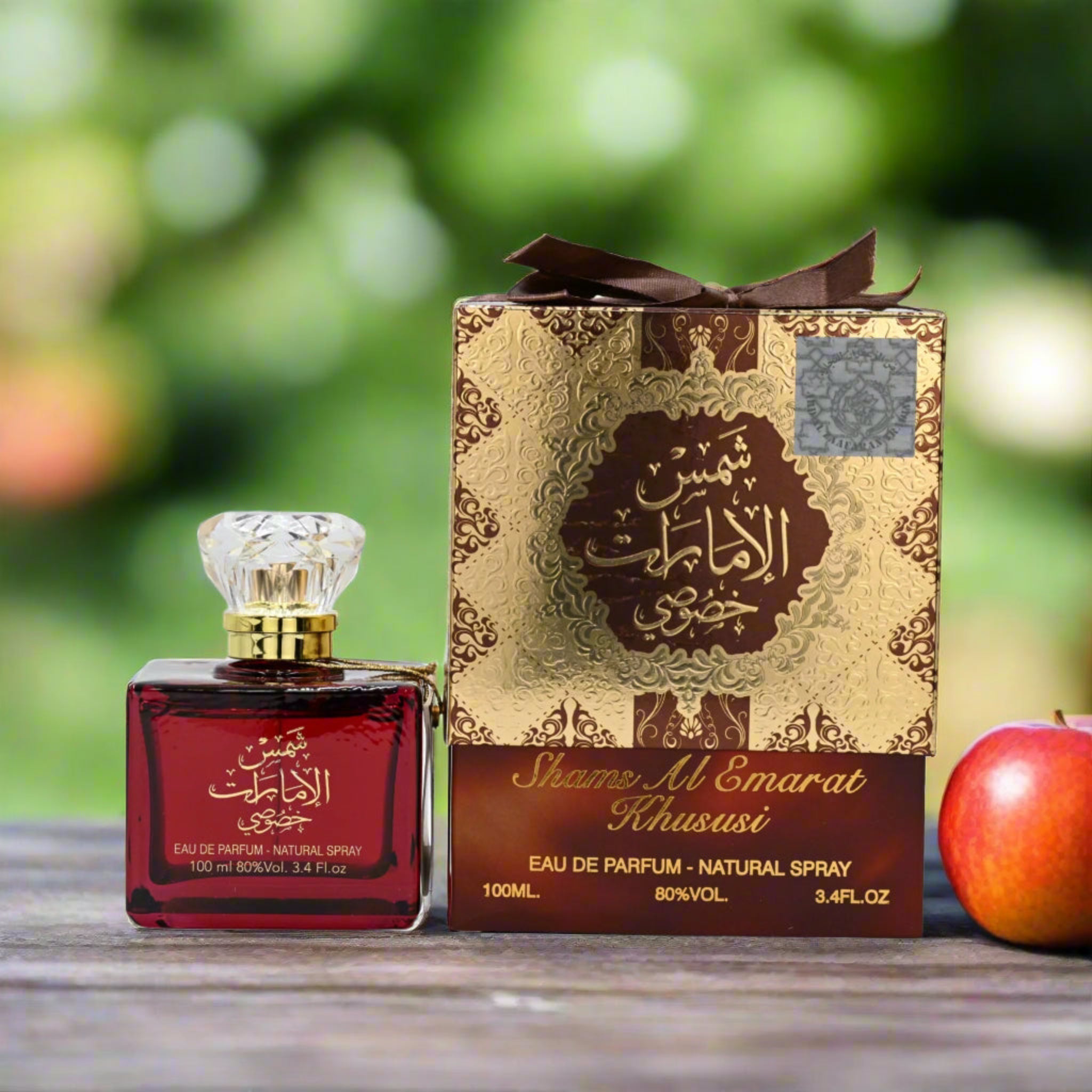Shams Al Emarat Khususi perfume bottle and packaging with an apple on a wooden surface.
