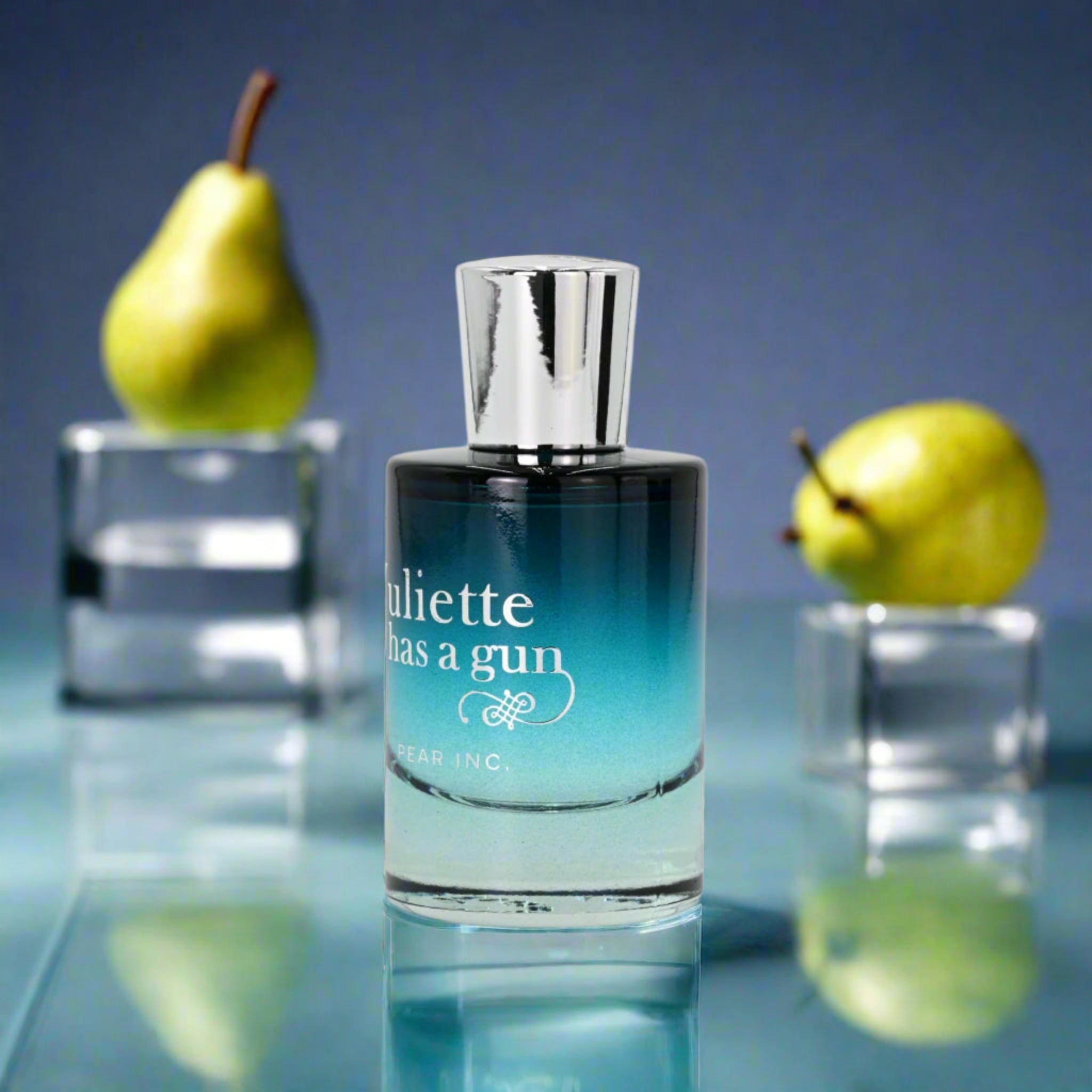 Perfume bottle labeled 'Juliette has a gun' with pears in the background on a reflective surface.