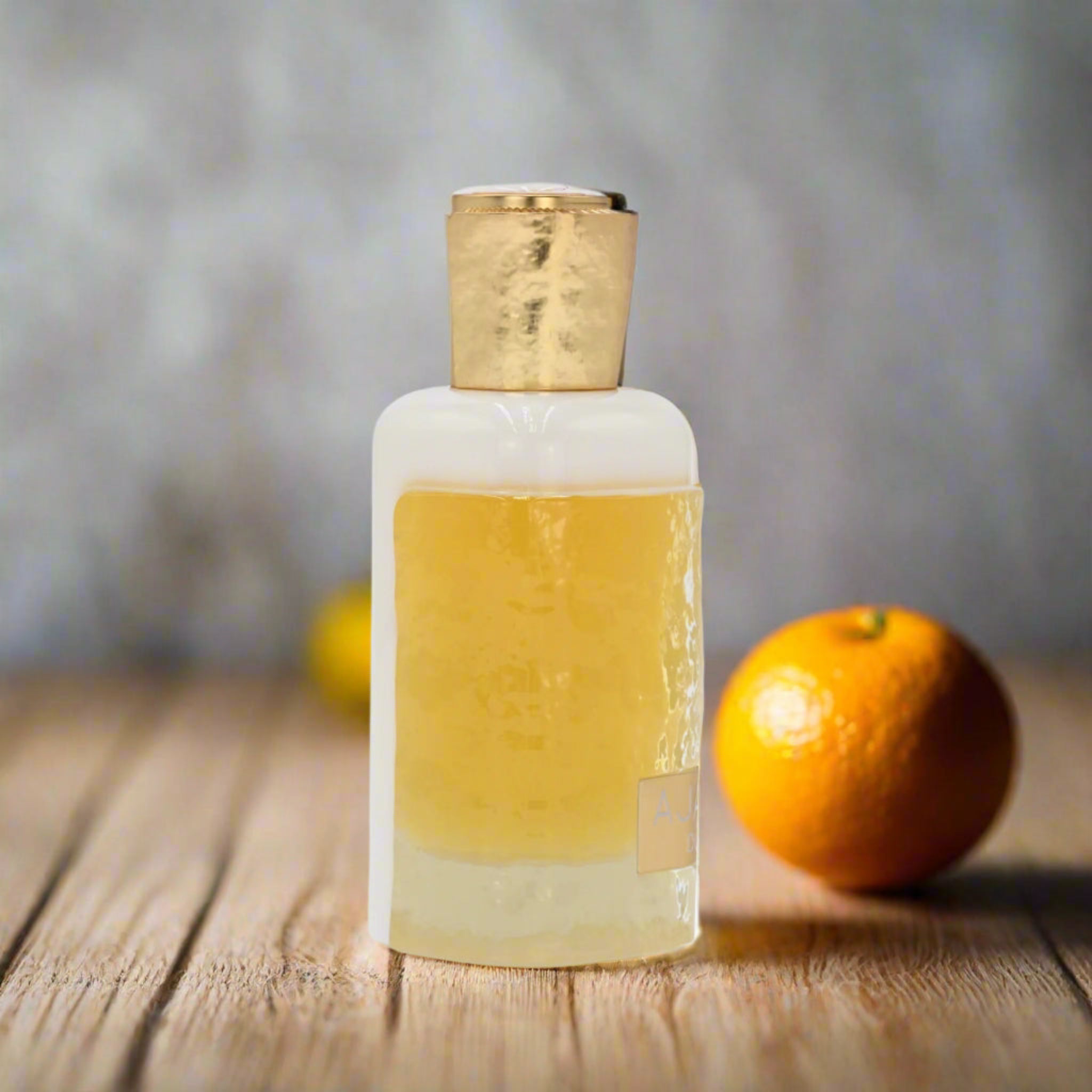 Bottle of clear liquid with a gold cap on a wooden surface, with an orange in the background.