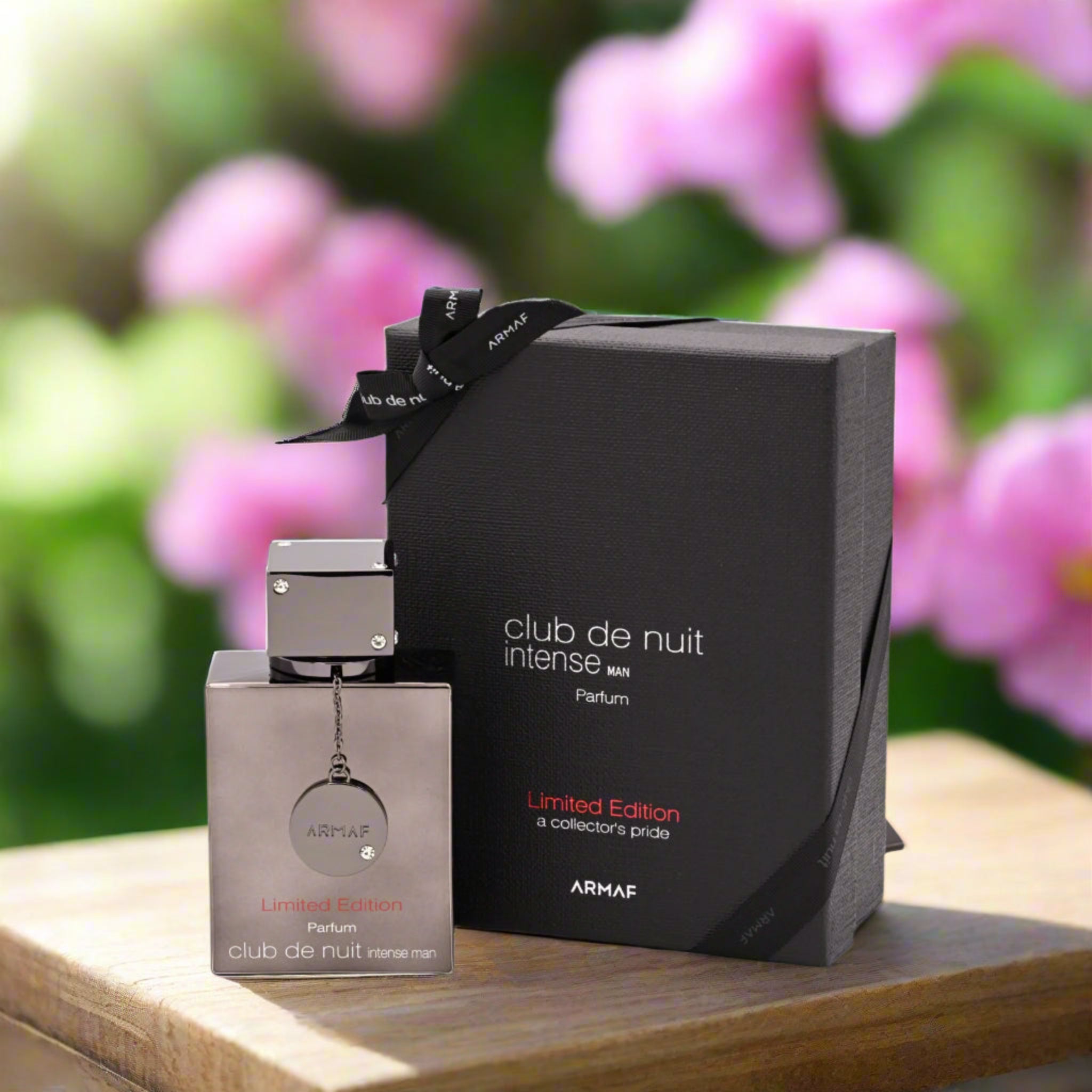 ARMé club de nuit intense perfume bottle and packaging on a wooden surface with blurred flowers in the background