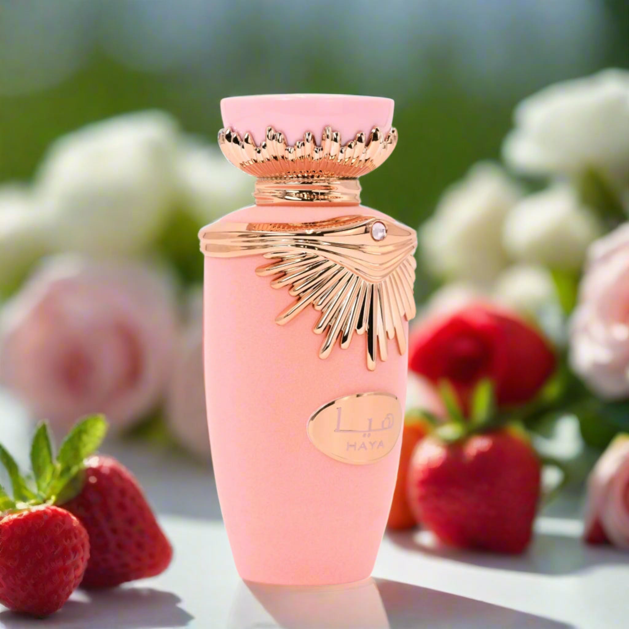Pink perfume bottle with gold accents on a surface with strawberries and flowers in the background