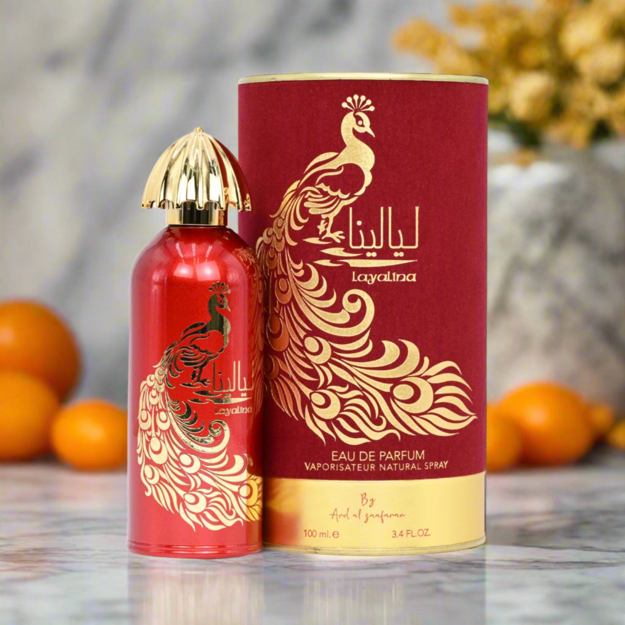 Red and gold Layalina perfume bottle and packaging with peacock design on a blurred background.
