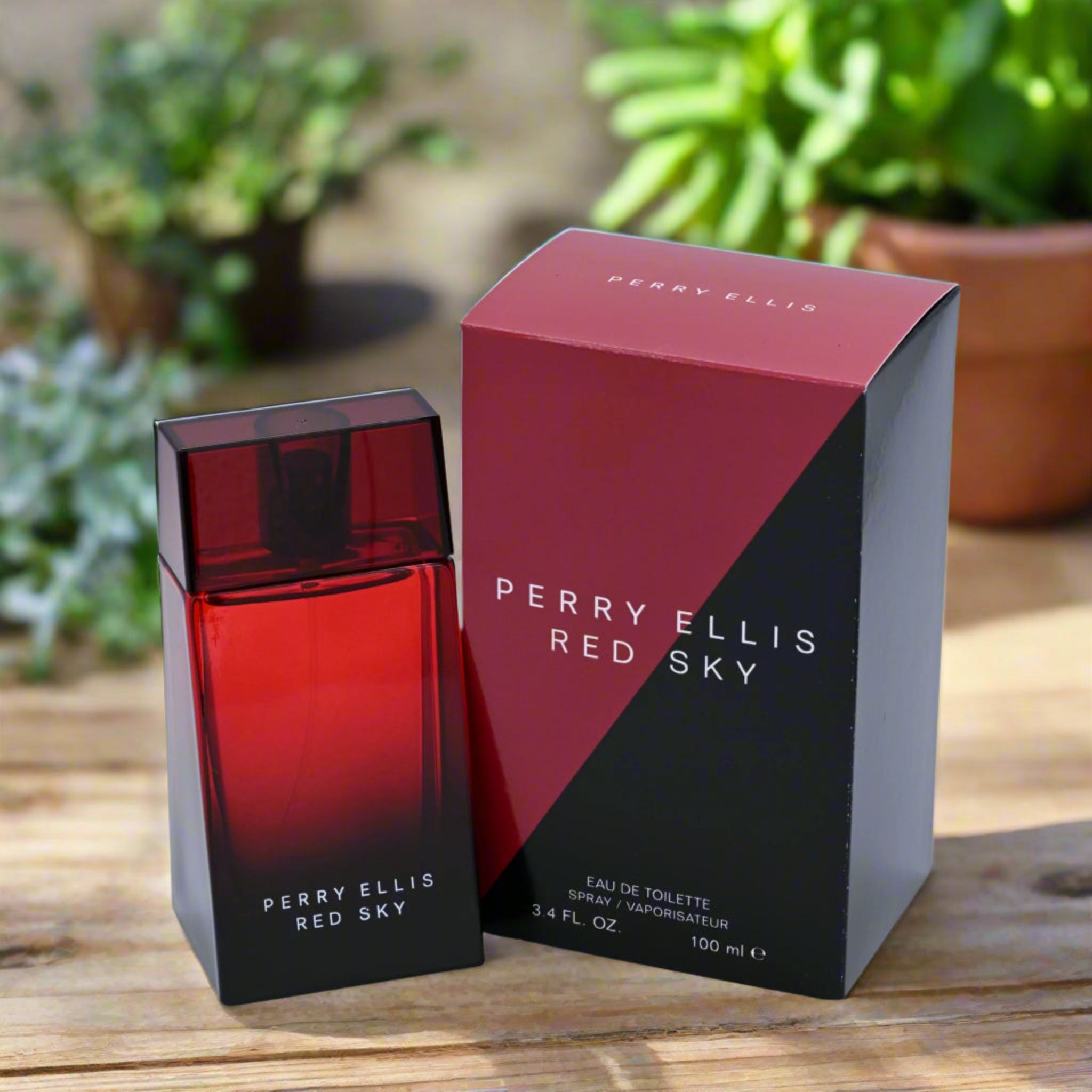 Perry Ellis Red Sky perfume bottle and packaging on a wooden surface with plants in the background