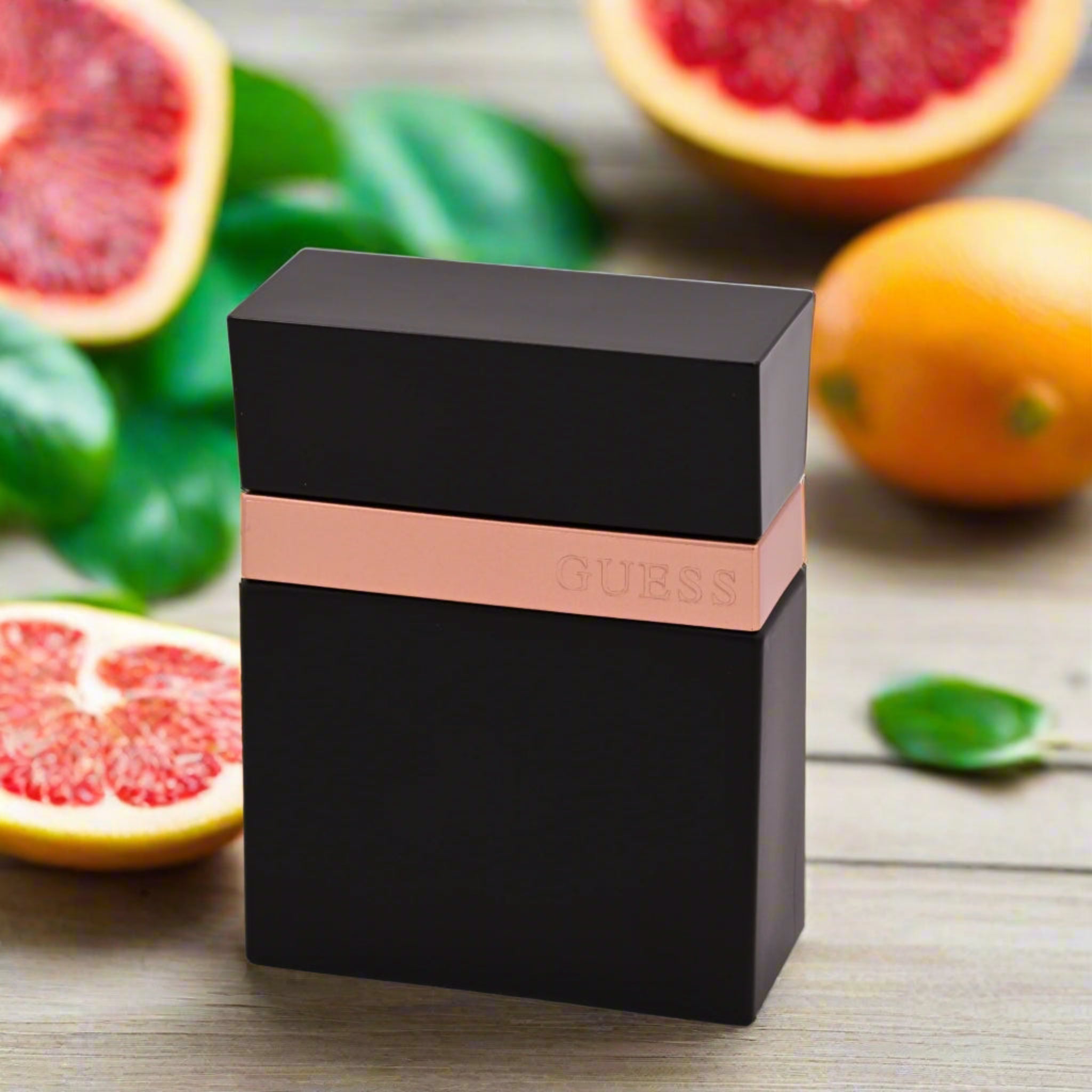 Black Guess perfume bottle with rose gold band on a wooden surface with grapefruits in the background
