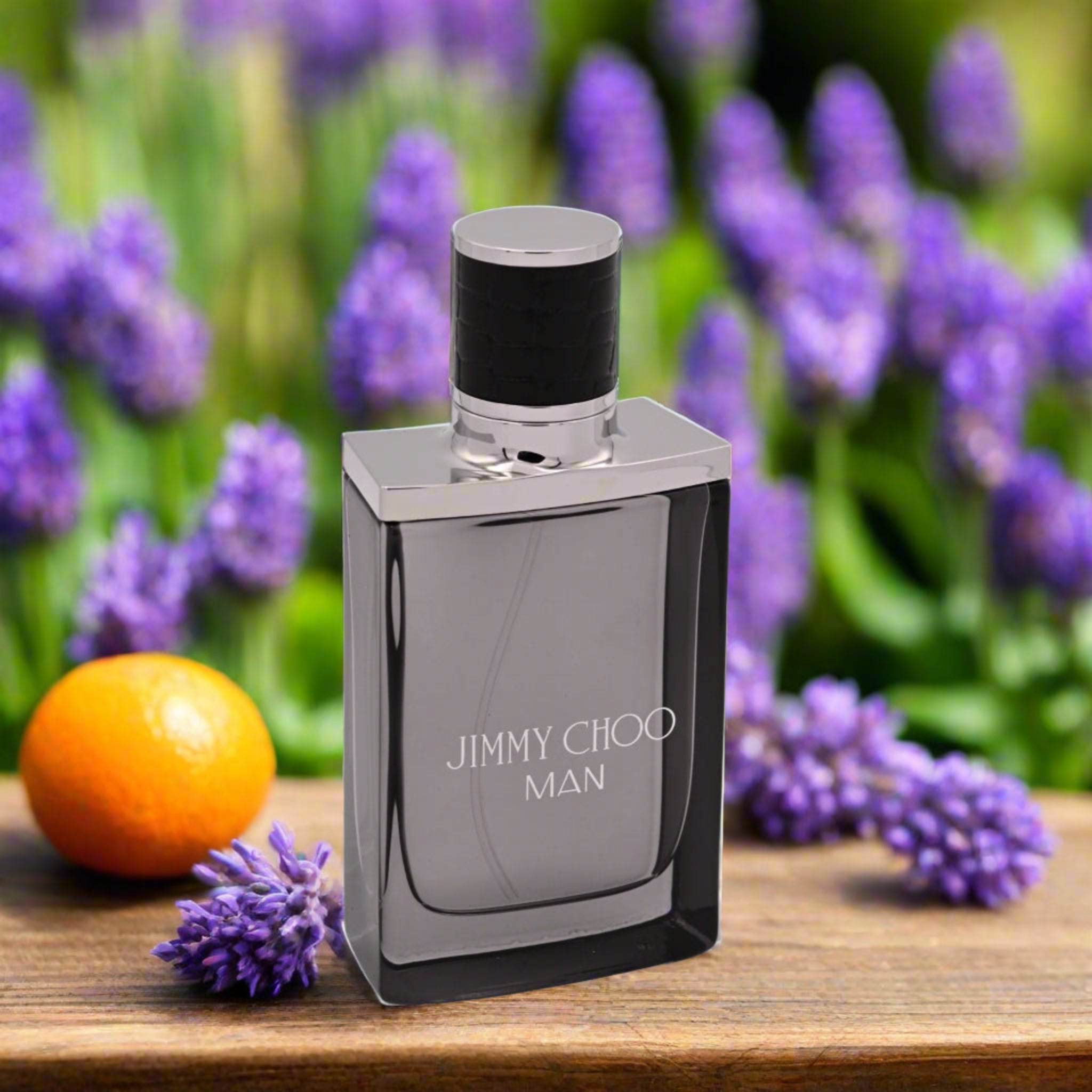 Jimmy Choo Man perfume bottle on a wooden surface with purple flowers and an orange in the background