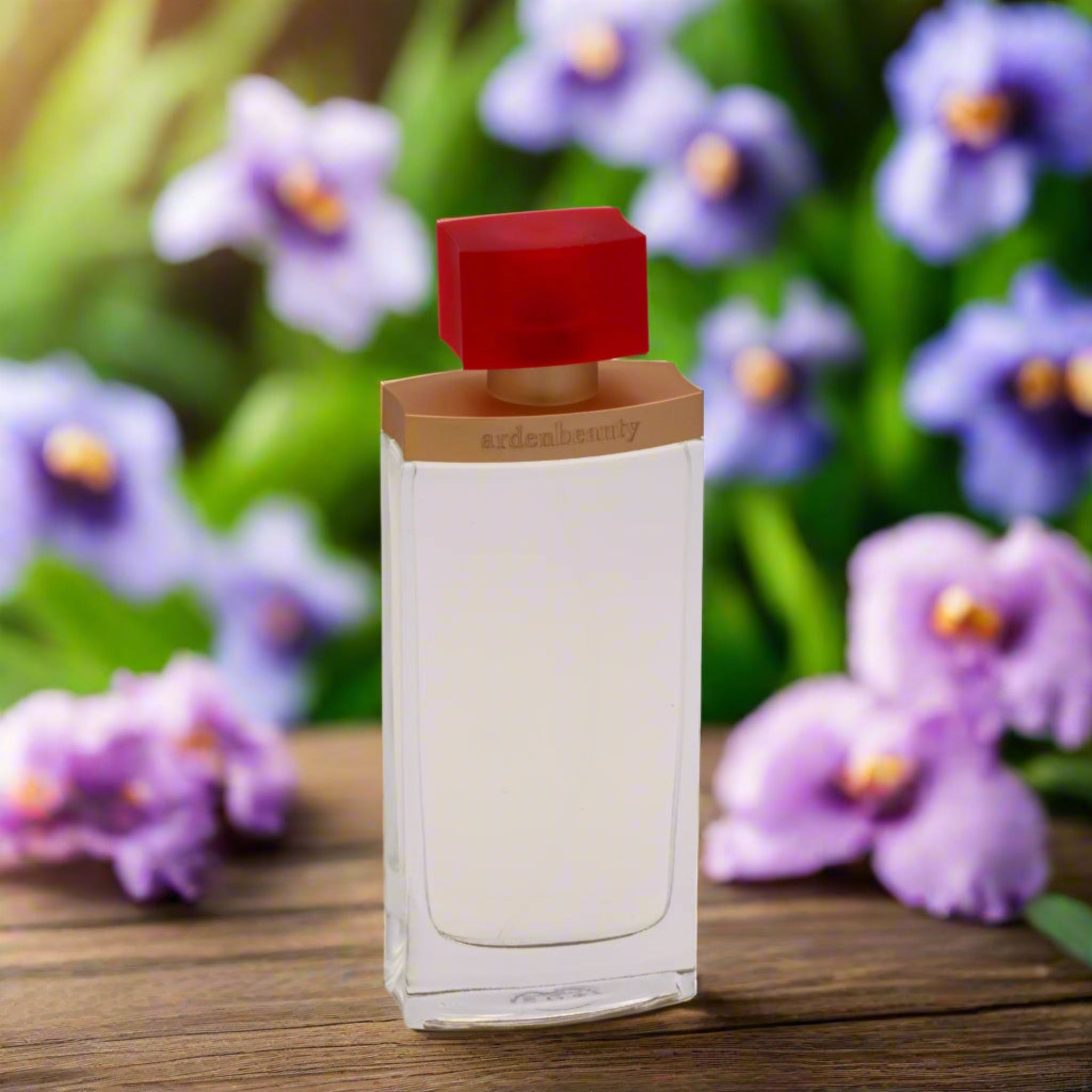Perfume bottle with a red cap on a wooden surface with purple flowers in the background