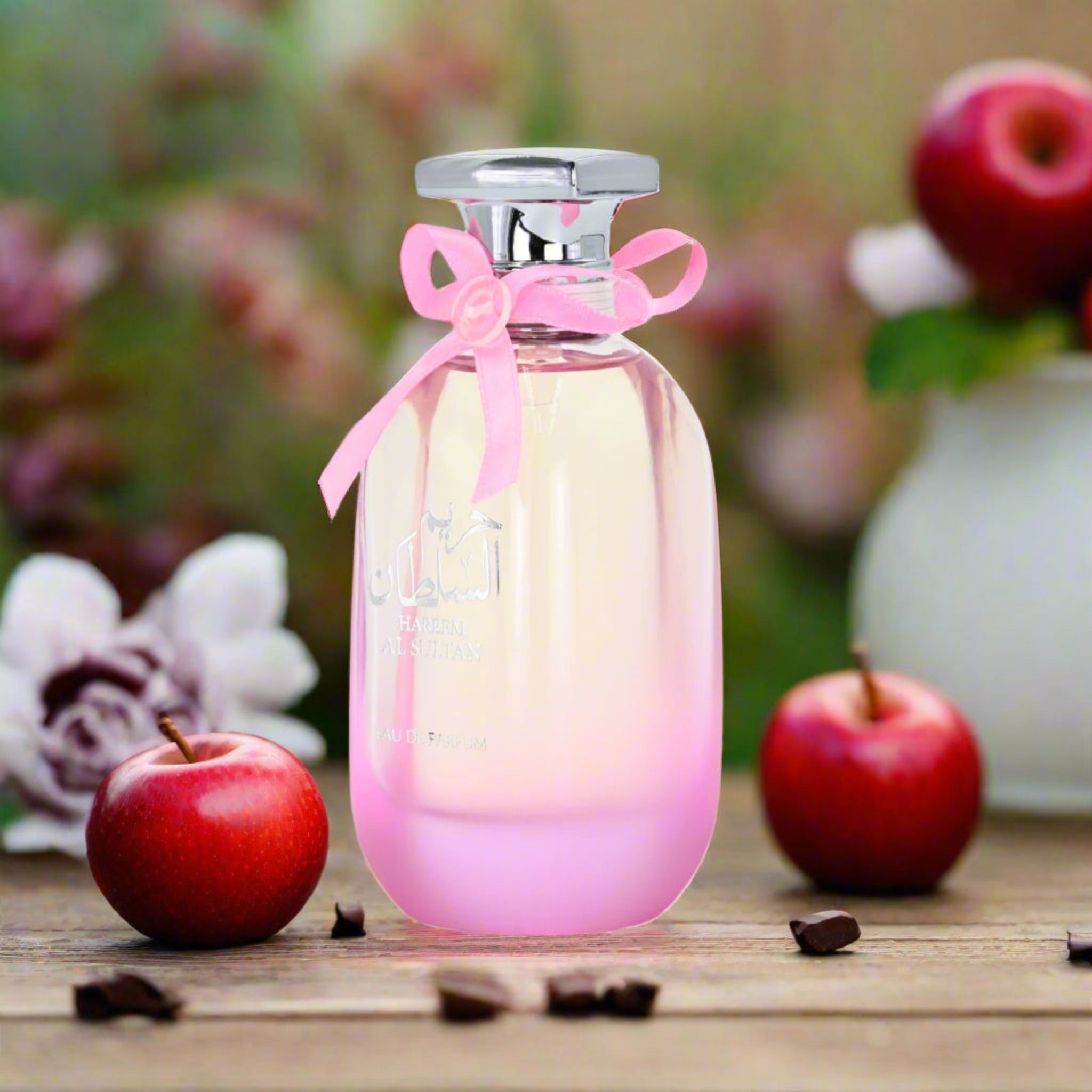Perfume bottle with a pink ribbon on a wooden surface with apples and flowers in the background