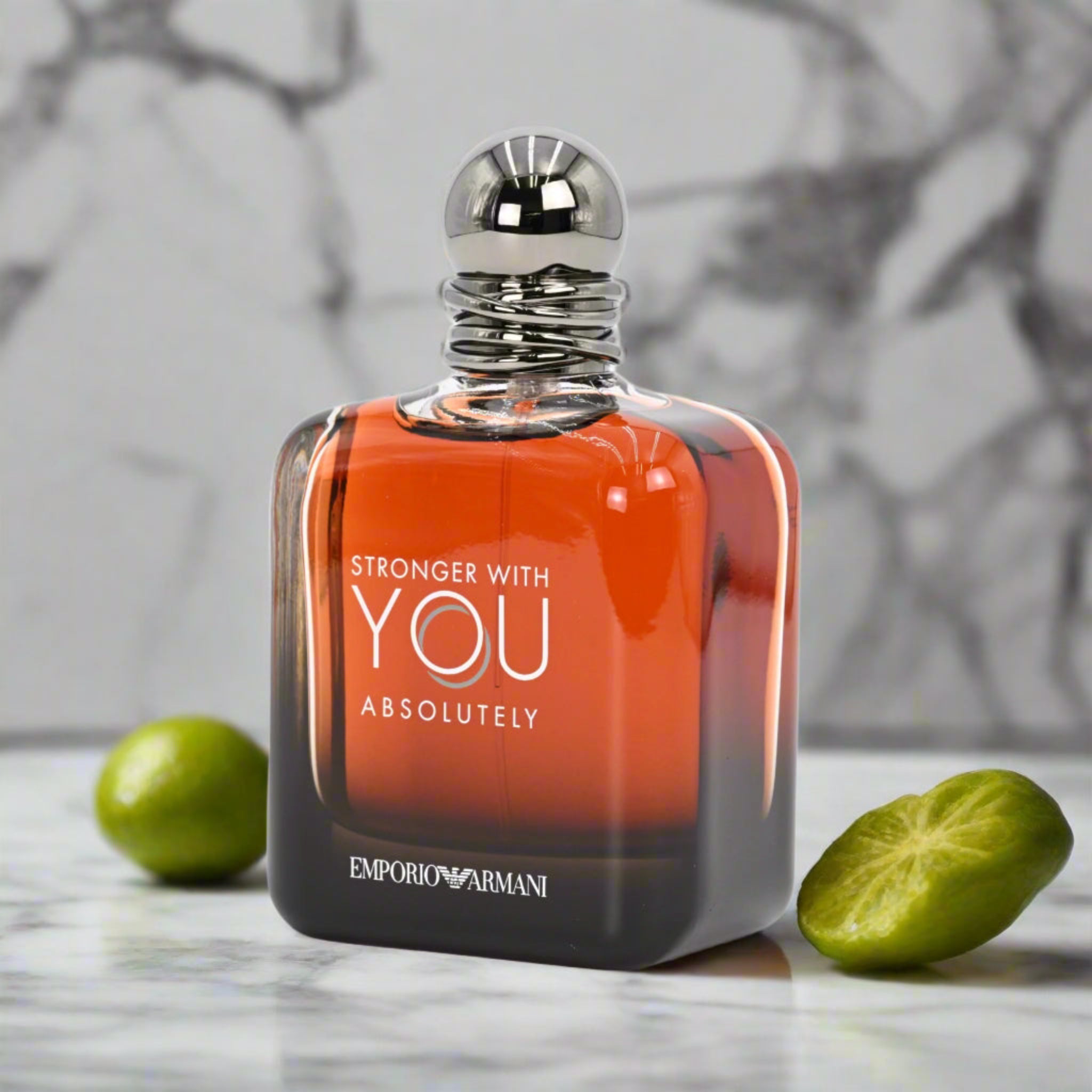 Perfume bottle with 'Stronger with You Absolutely' text and Emporio Armani logo on a marble surface with limes.