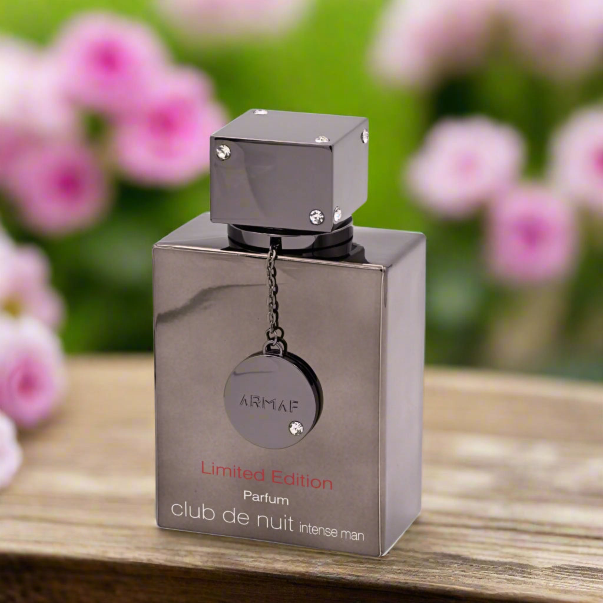 Silver Armaf perfume bottle on a wooden surface with pink flowers in the background