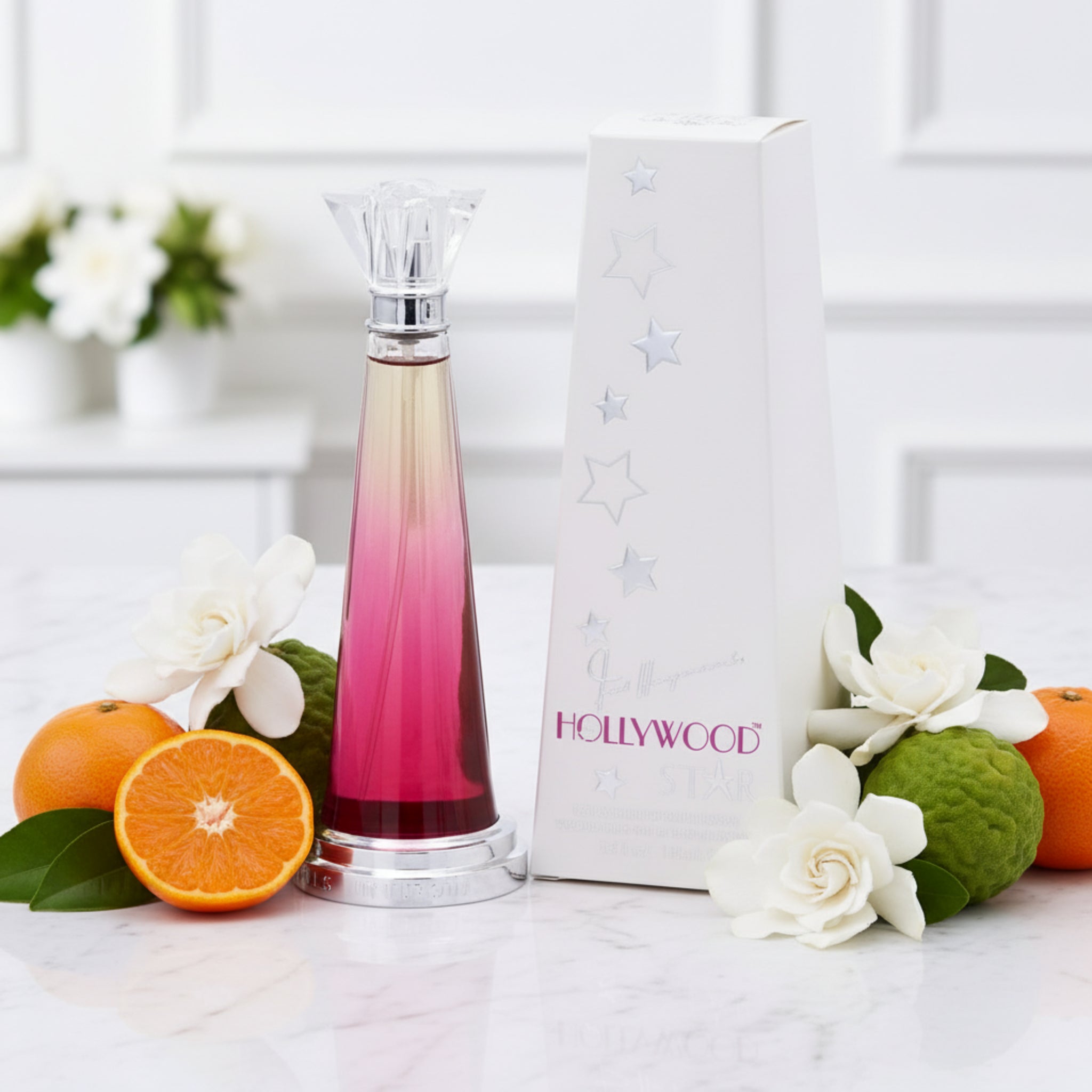 Perfume bottle with 'Hollywood' packaging, oranges, and flowers on a white surface.