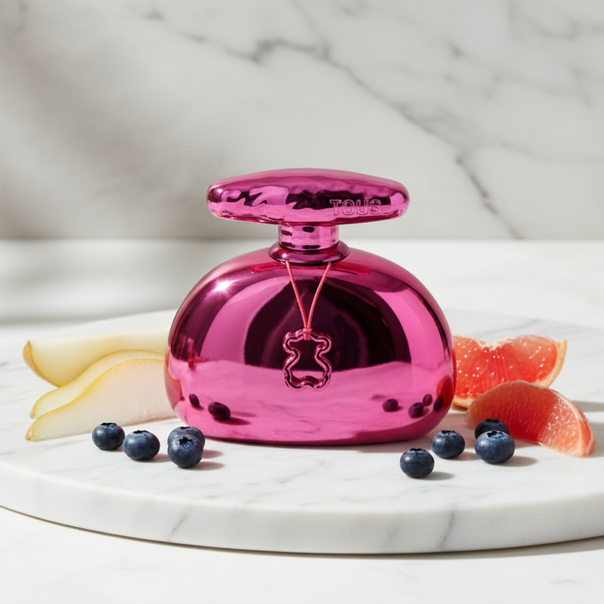 Shiny pink perfume bottle with 'Tous' branding on a white background