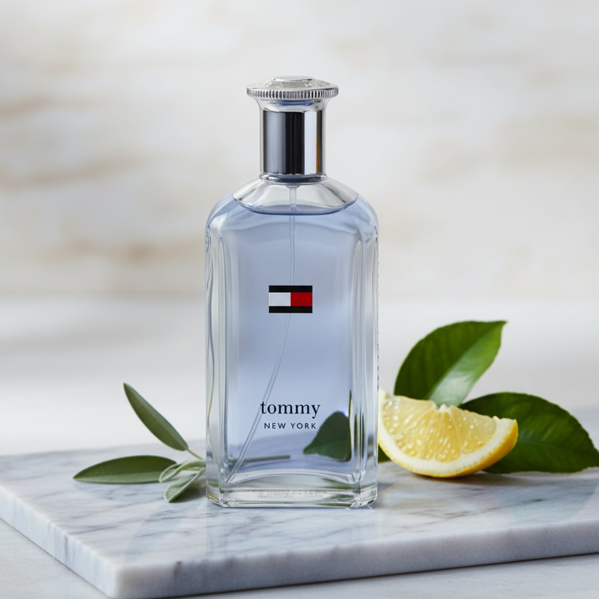Tommy New York perfume bottle with lemon slices and leaves on a marble surface