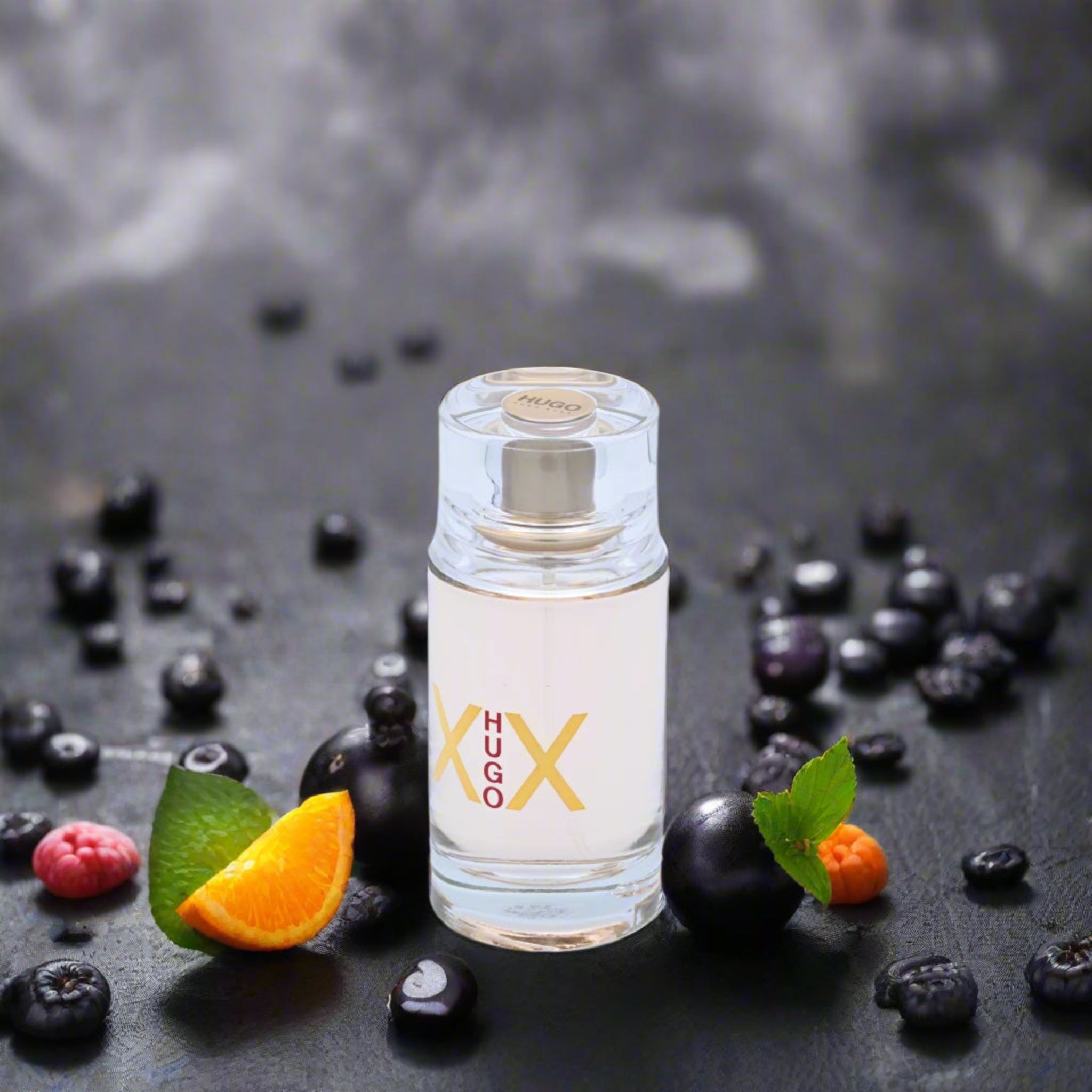 Perfume bottle labeled 'Hugo' surrounded by fruits and berries on a dark background