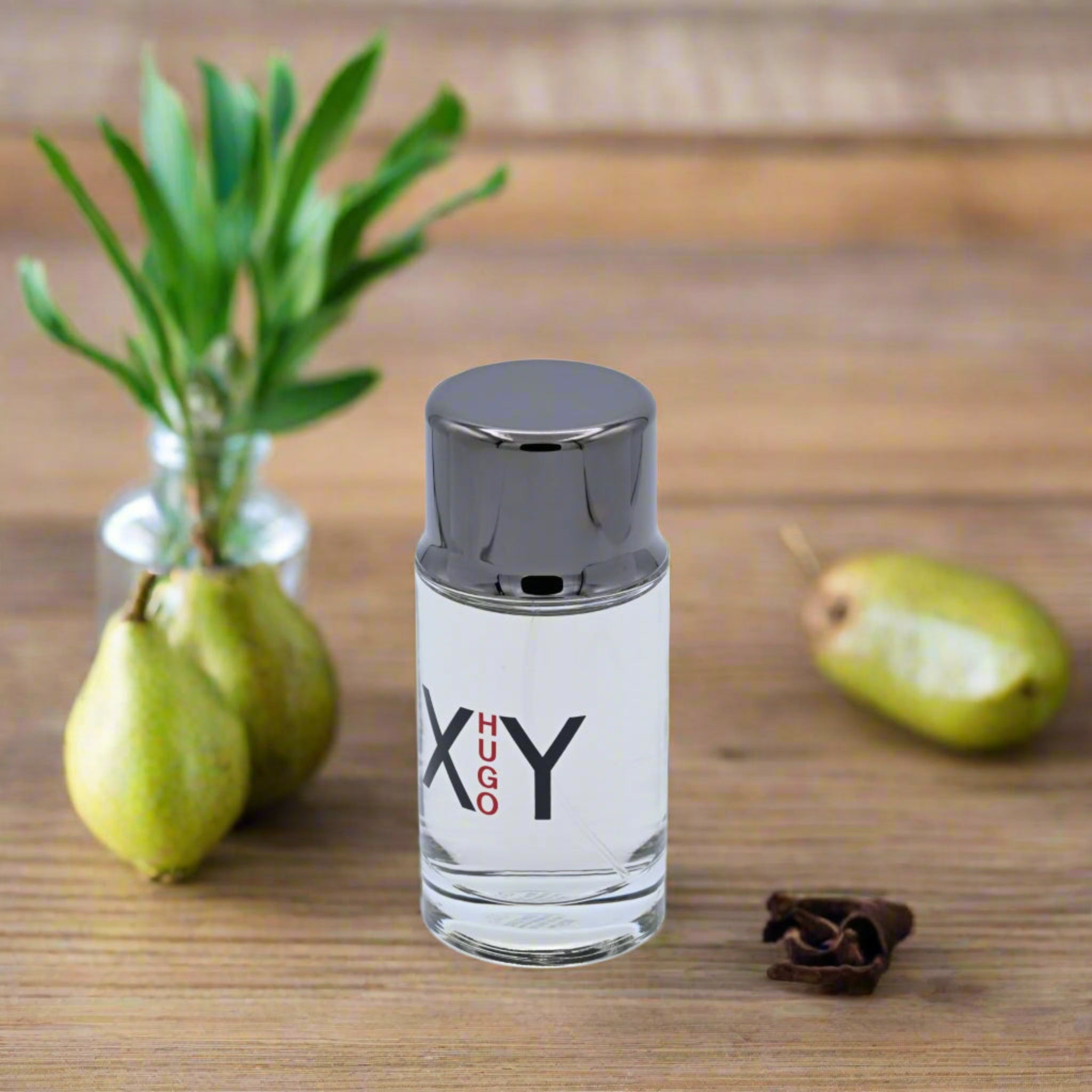 Perfume bottle labeled 'XY' on a wooden surface with pears and a plant.