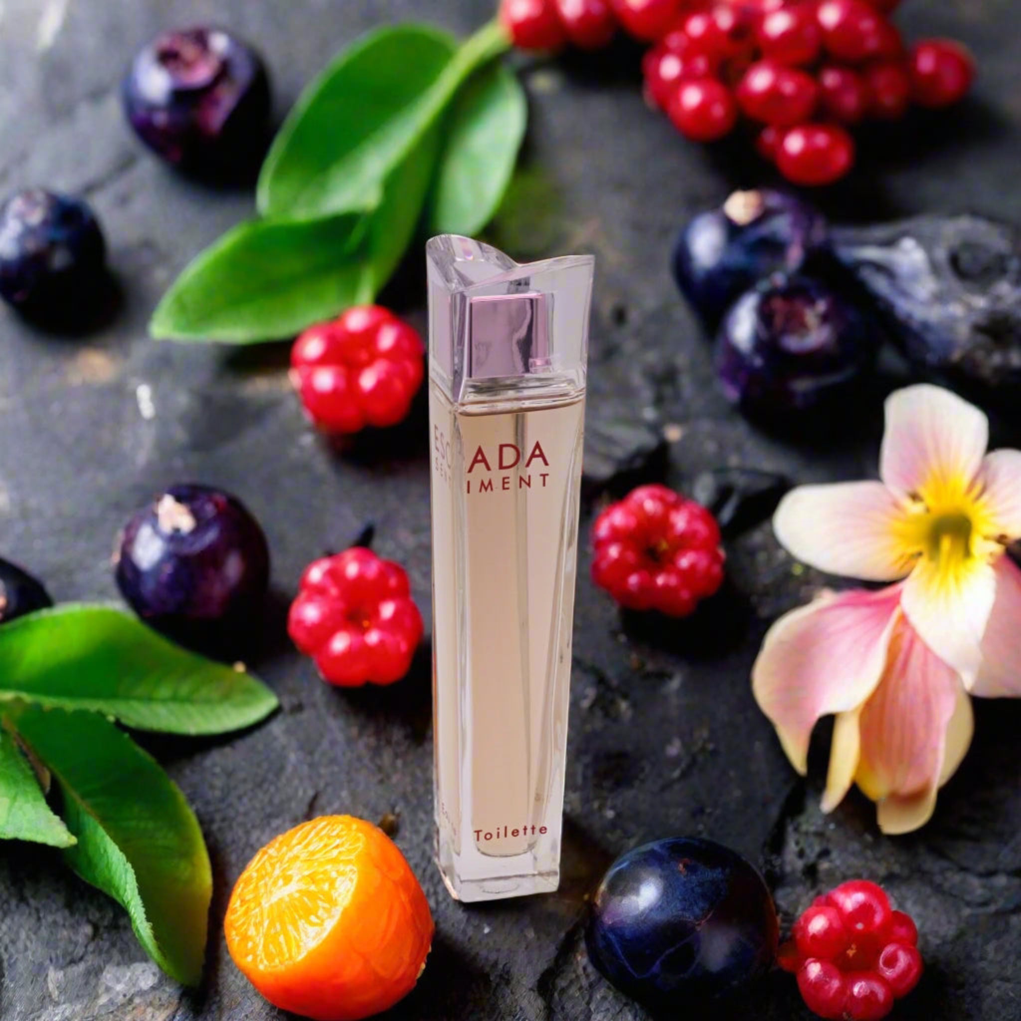 Escada Sentiment perfume bottle surrounded by fruits and flowers on a dark surface