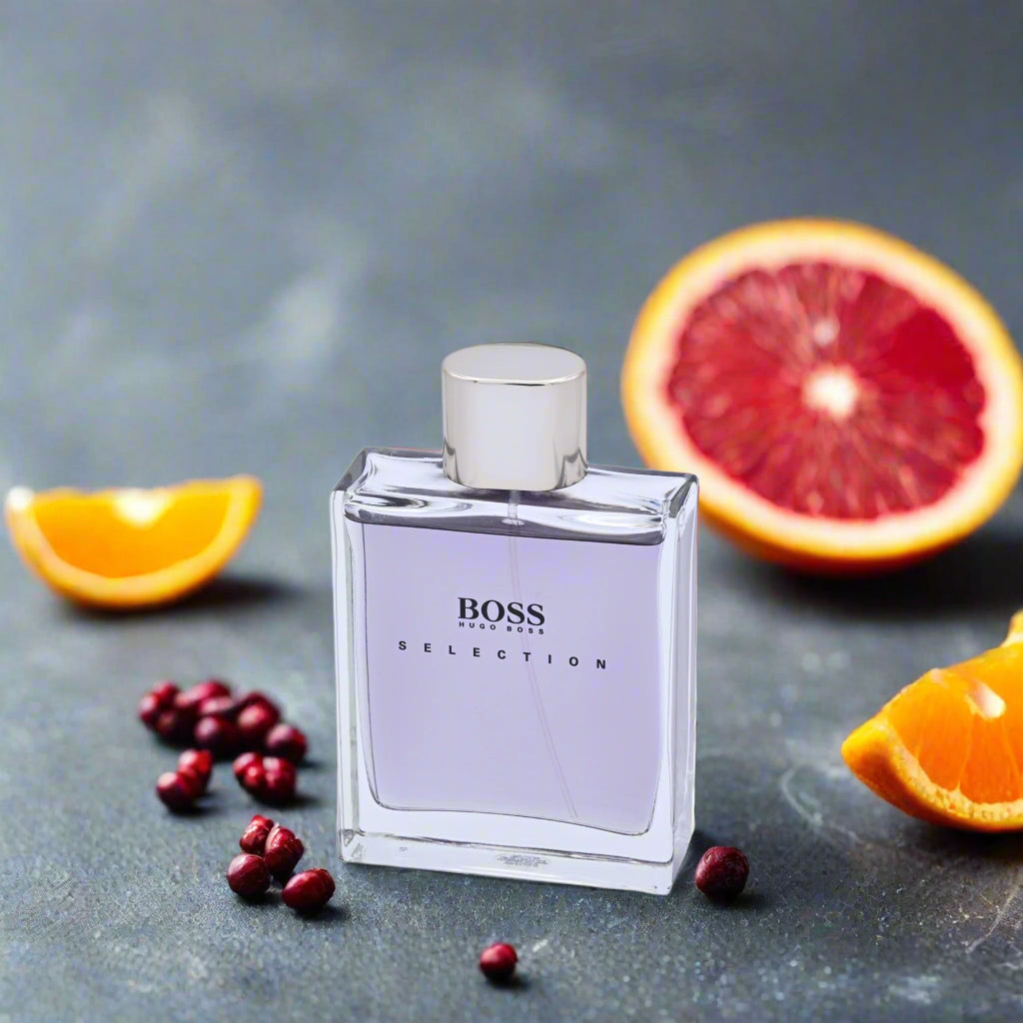 BOSS perfume bottle with oranges and pomegranate seeds on a gray background