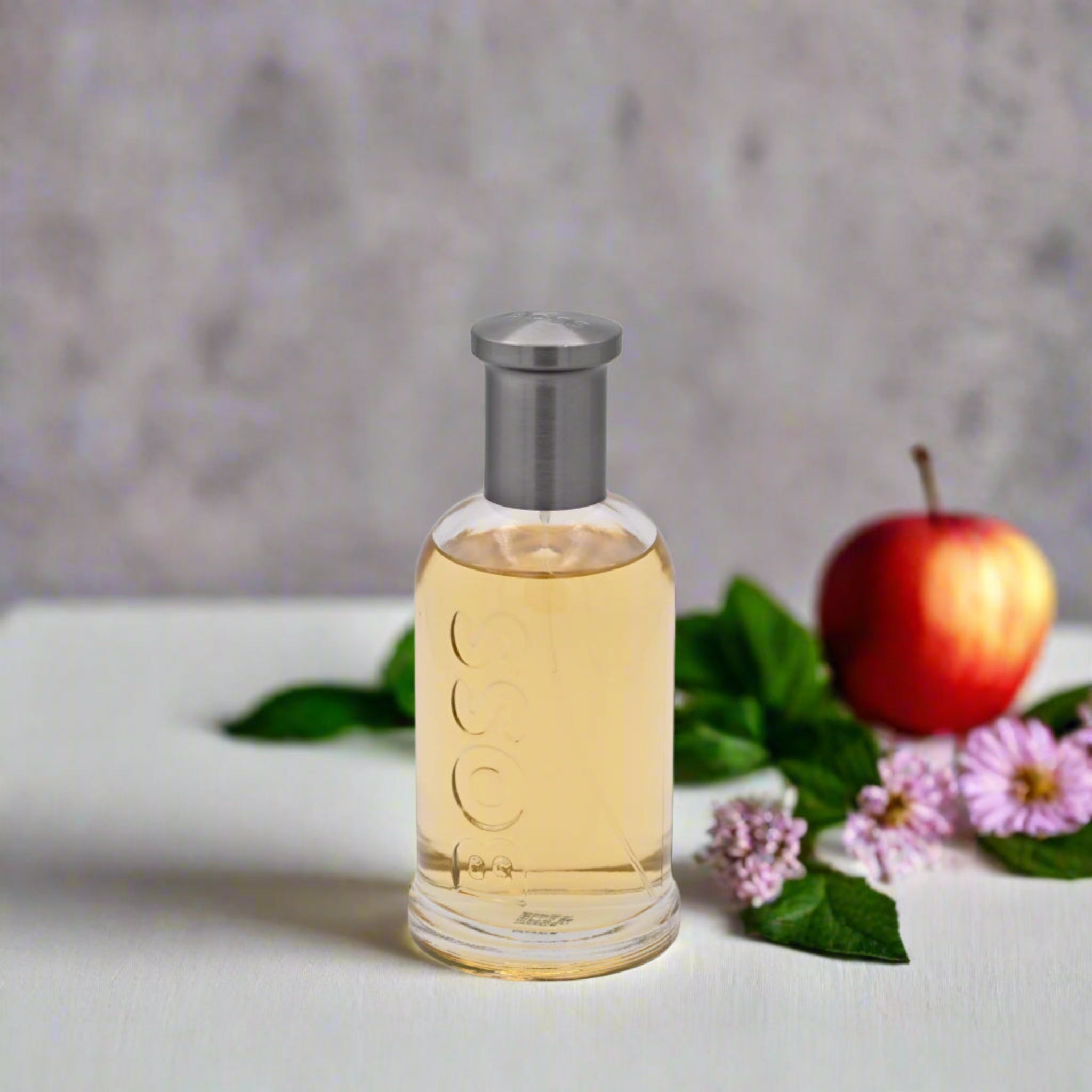 Bottle of perfume with an apple and flowers on a light surface