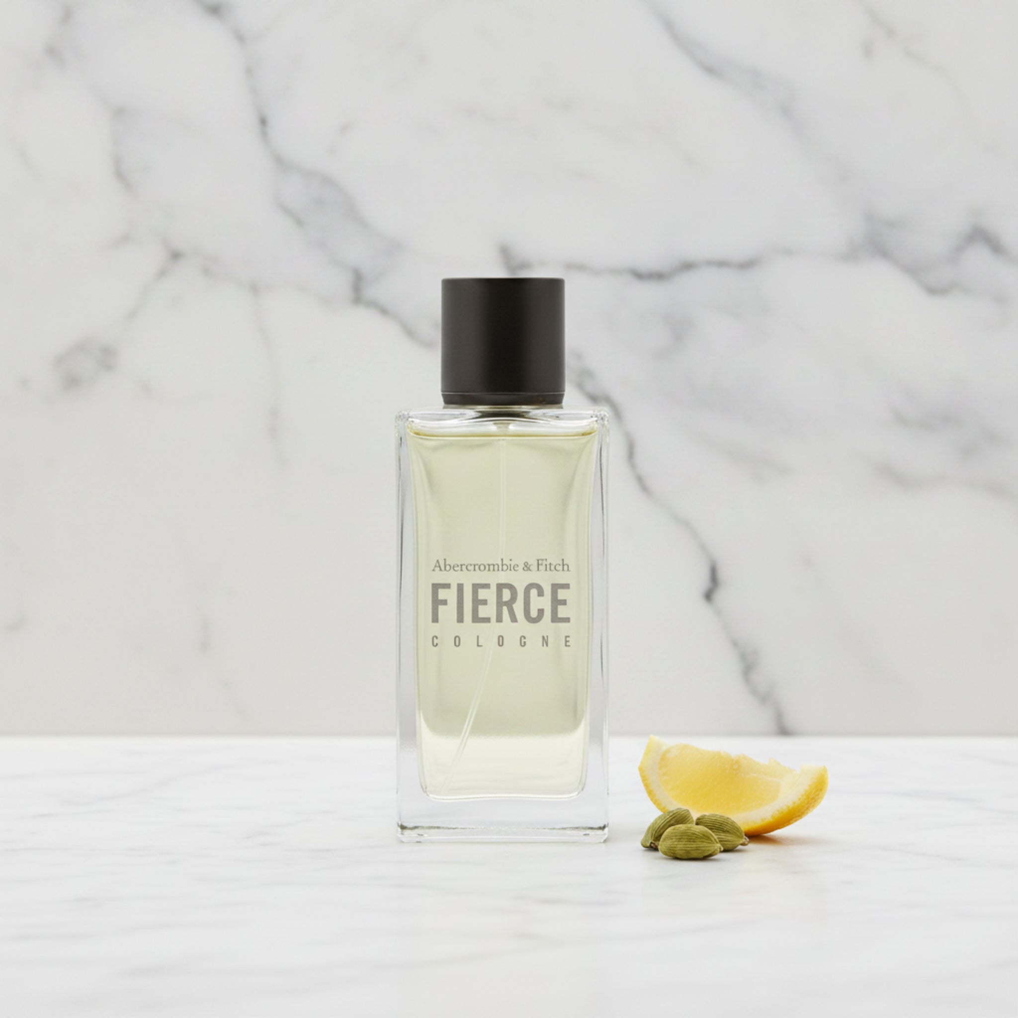A bottle of Abercrombie & Fitch Fierce cologne on a marble surface with a lemon and cardamom pods.