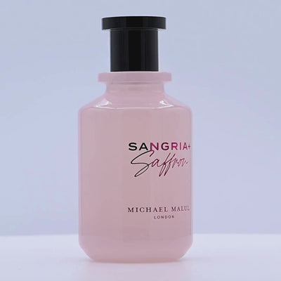 Perfume bottle labeled 'Sangria + Saffron' by Michael Malul rotating on a white podium