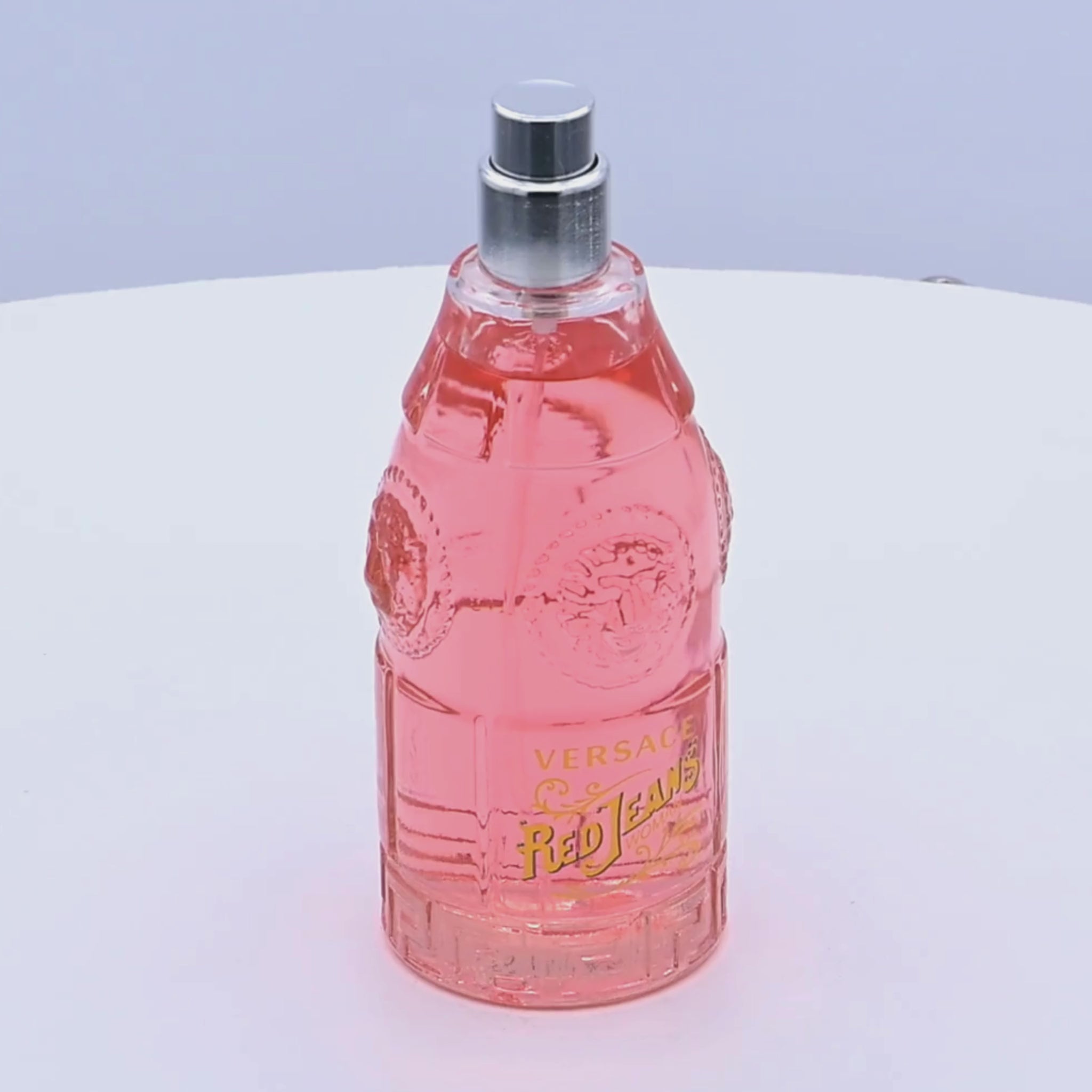 Pink Versace Red Jeans perfume bottle rotating on a white podium