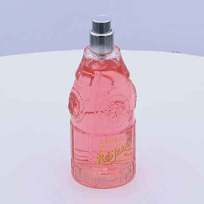Pink Versace Red Jeans perfume bottle rotating on a white podium