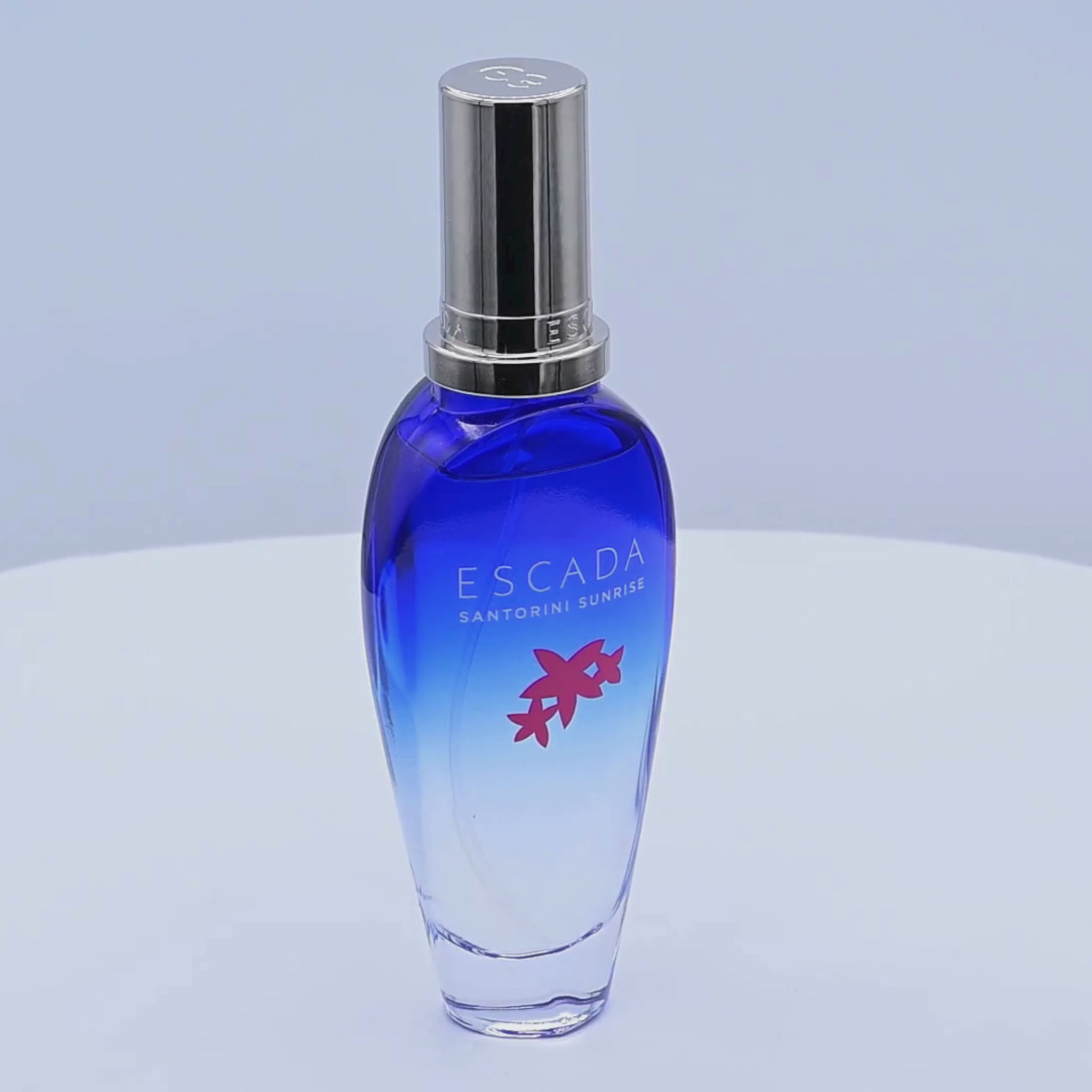 Escada Santorini Sunrise perfume bottle rotating on a white podium