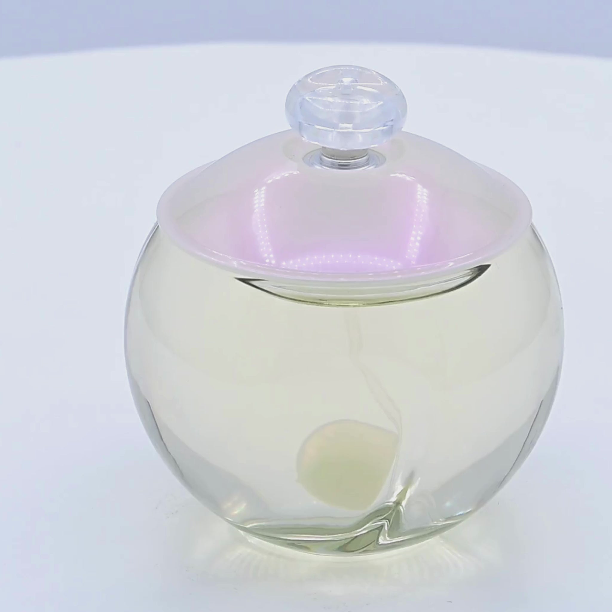 Clear glass perfume bottle with a white lid rotating on a white podium