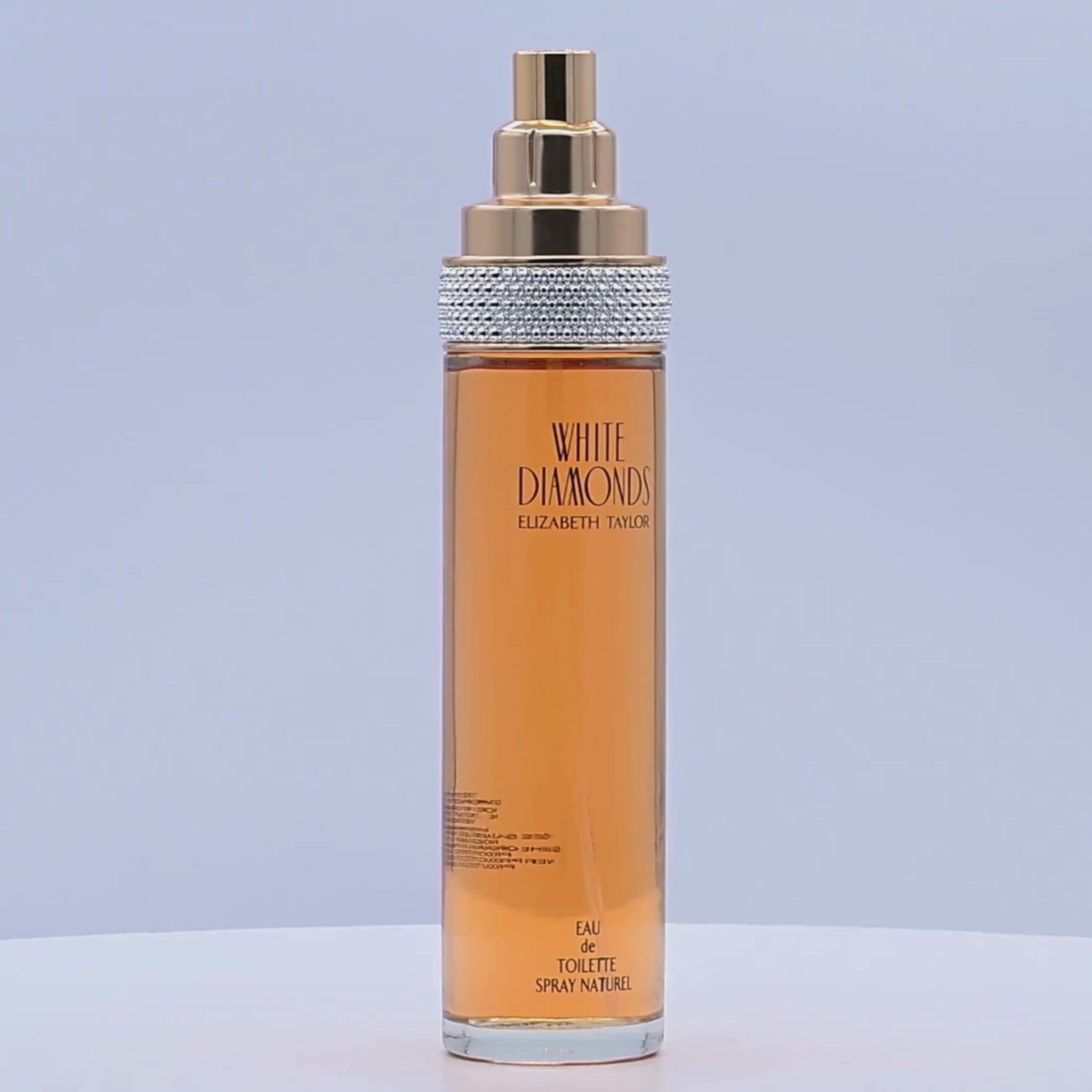 Perfume bottle with gold and silver cap rotating on a white podium