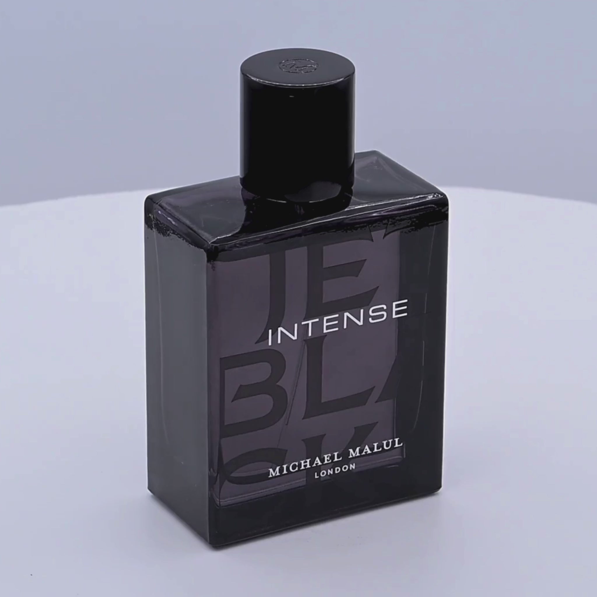 Black perfume bottle labeled 'INTENSE' by Michael Malul rotating on a white podium