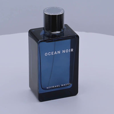 Blue perfume bottle labeled 'Ocean Noir' by Michael Malul rotating on a white podium