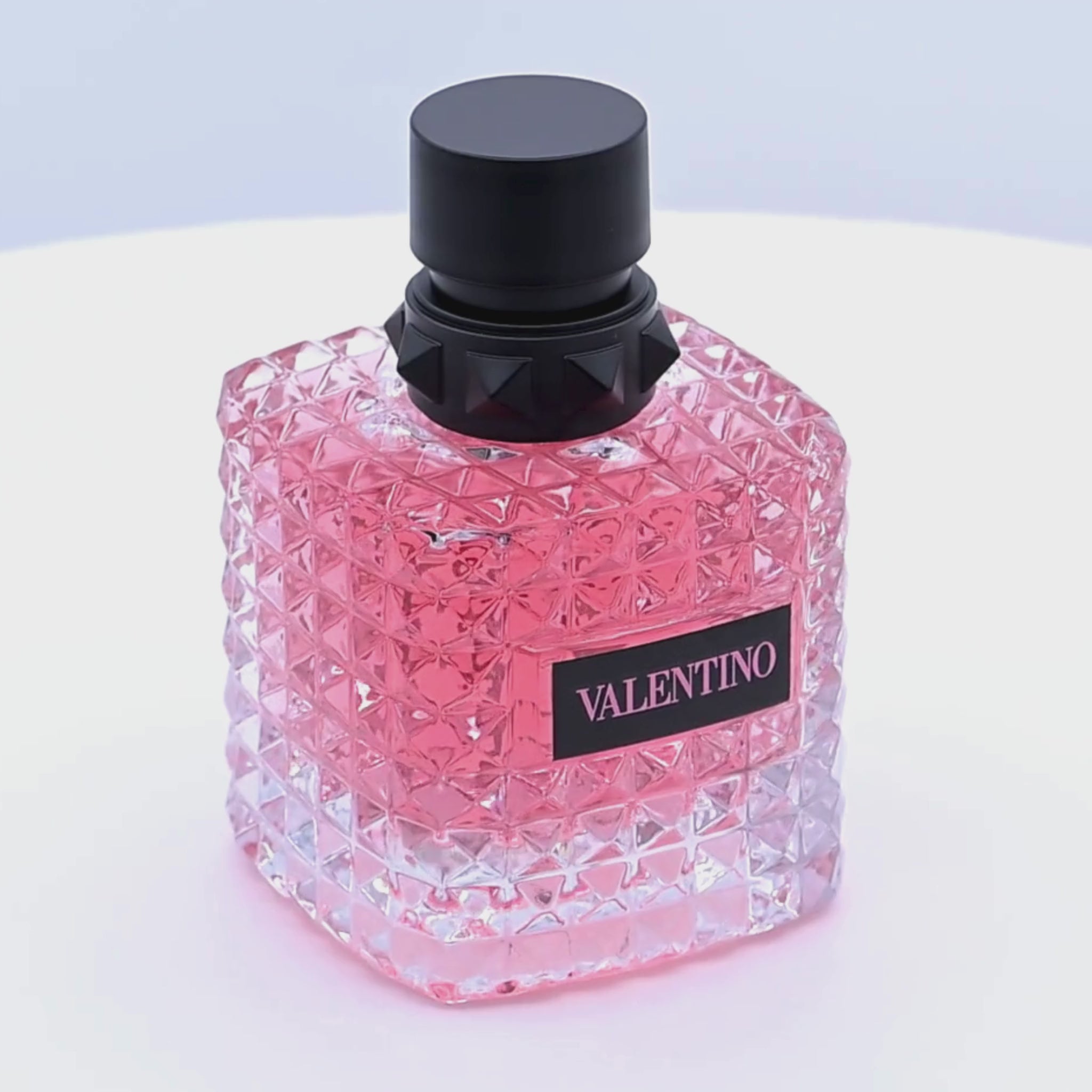 Pink Valentina perfume bottle with black cap rotating on a white podium
