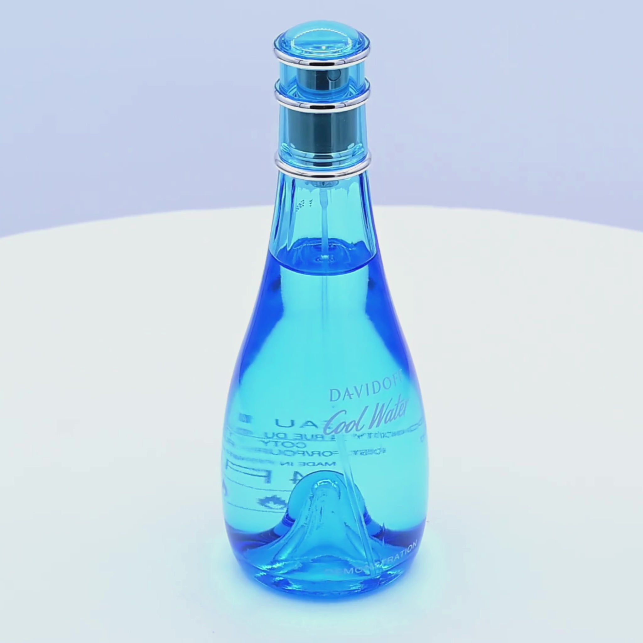 Blue perfume bottle with a spray nozzle rotating on a white podium